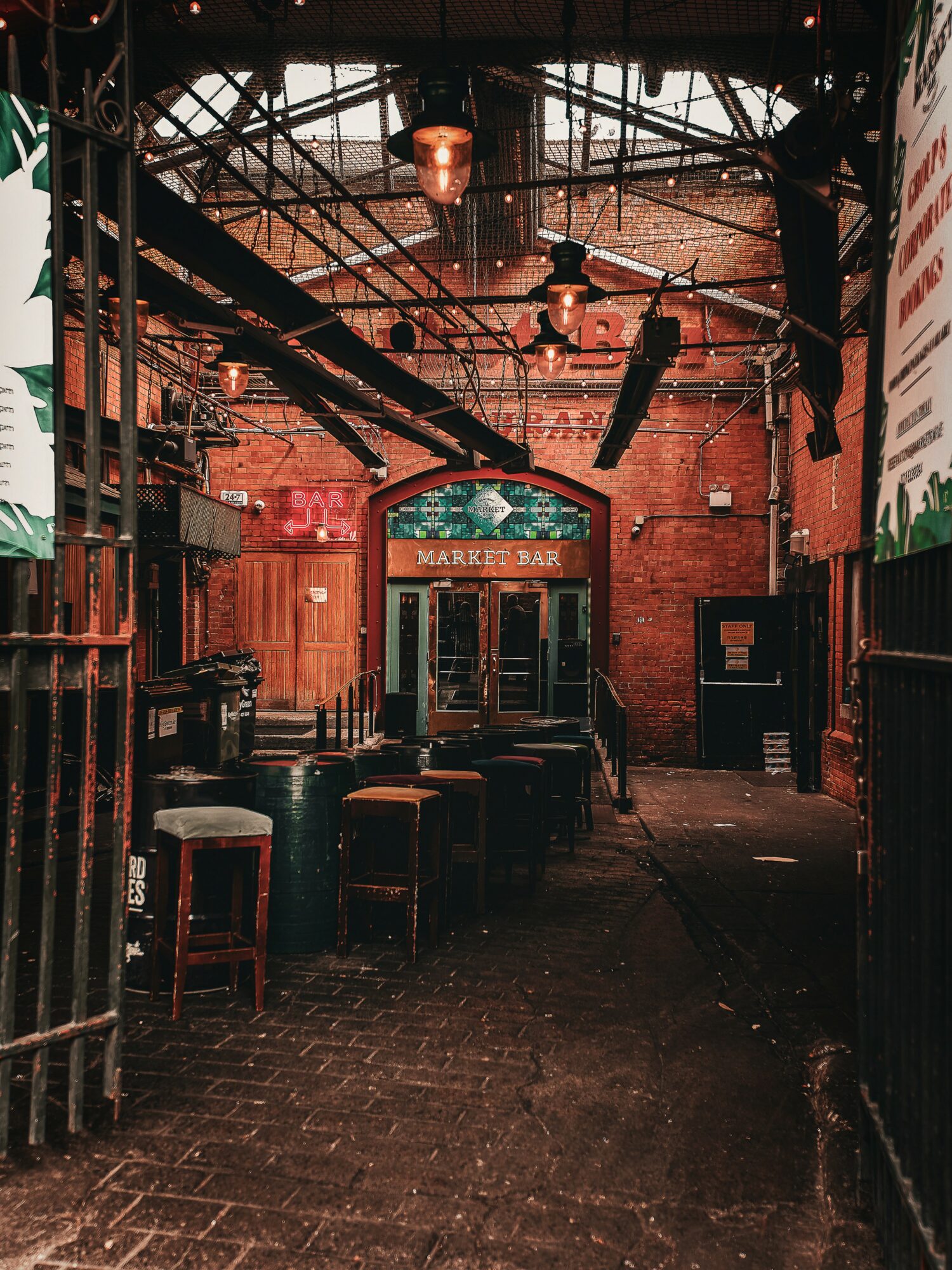 Indoor bar with brick walls, wooden furniture, and industrial ceiling, dimly lit with a sign reading 'Market Bar' above the entrance.