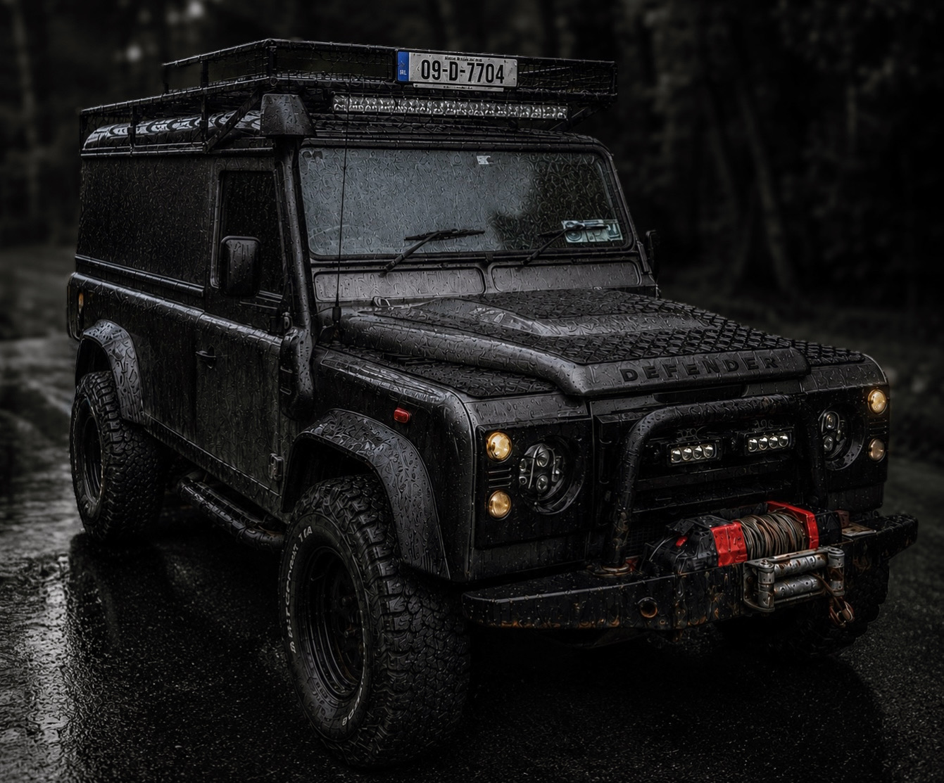 Black off-road vehicle parked on wet road, with a license plate and a roof rack, in a dark outdoor setting.