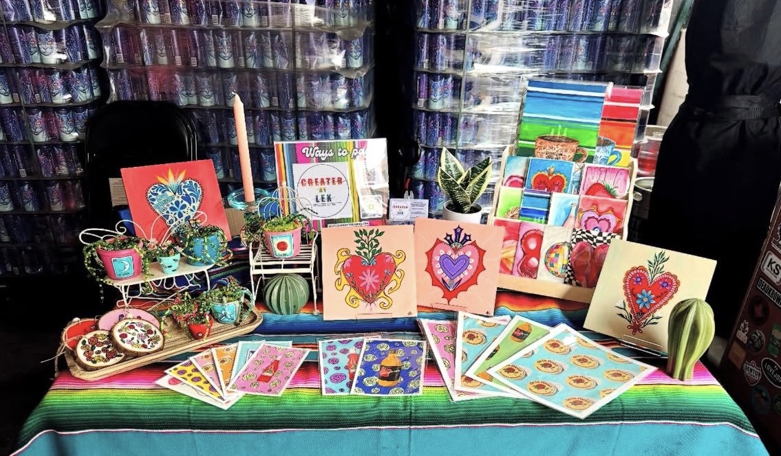 Display of colorful Valentine's Day cards, small gifts, and decorations on a table with a rainbow cloth, background of shelves.