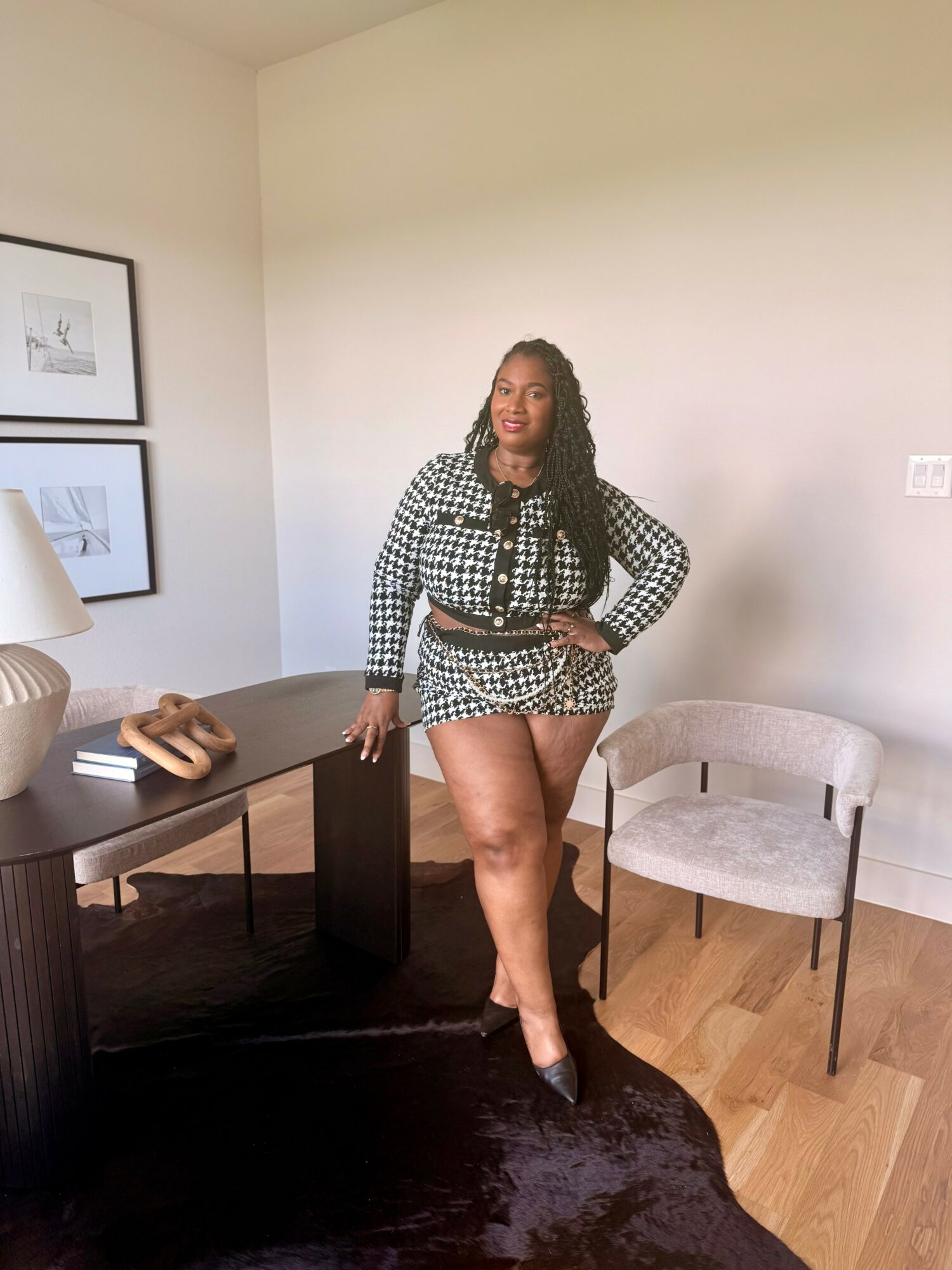 Woman standing in a room with a chair, desk, and framed pictures on the wall, smiling at the camera.