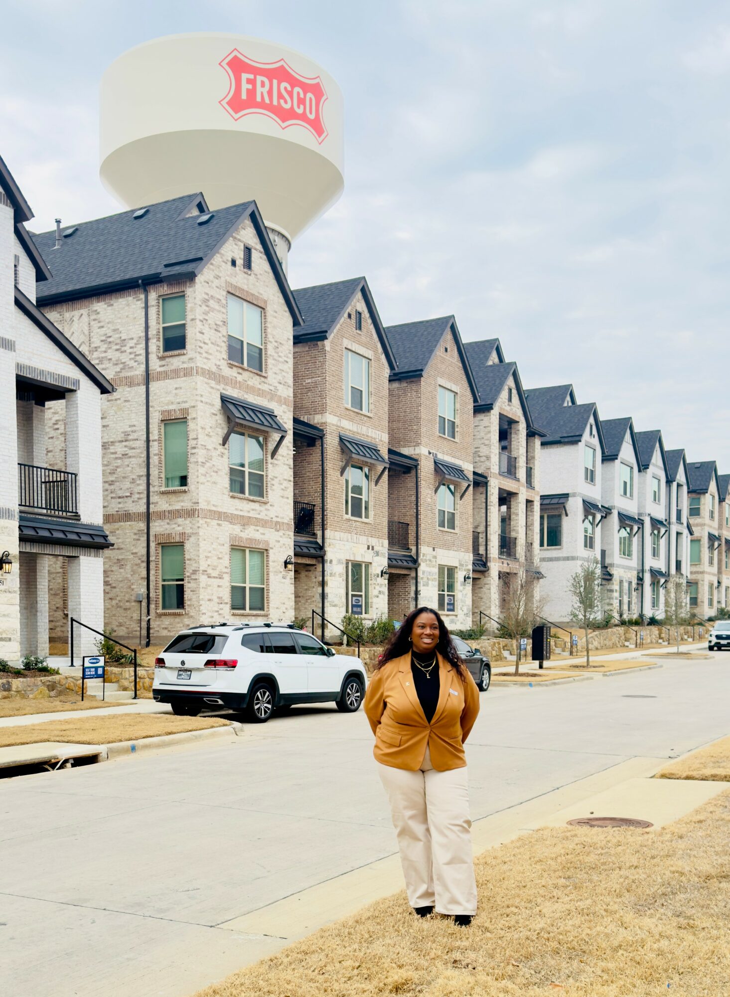 Person standing on sidewalk in front of row of modern apartment buildings with water tower in background.