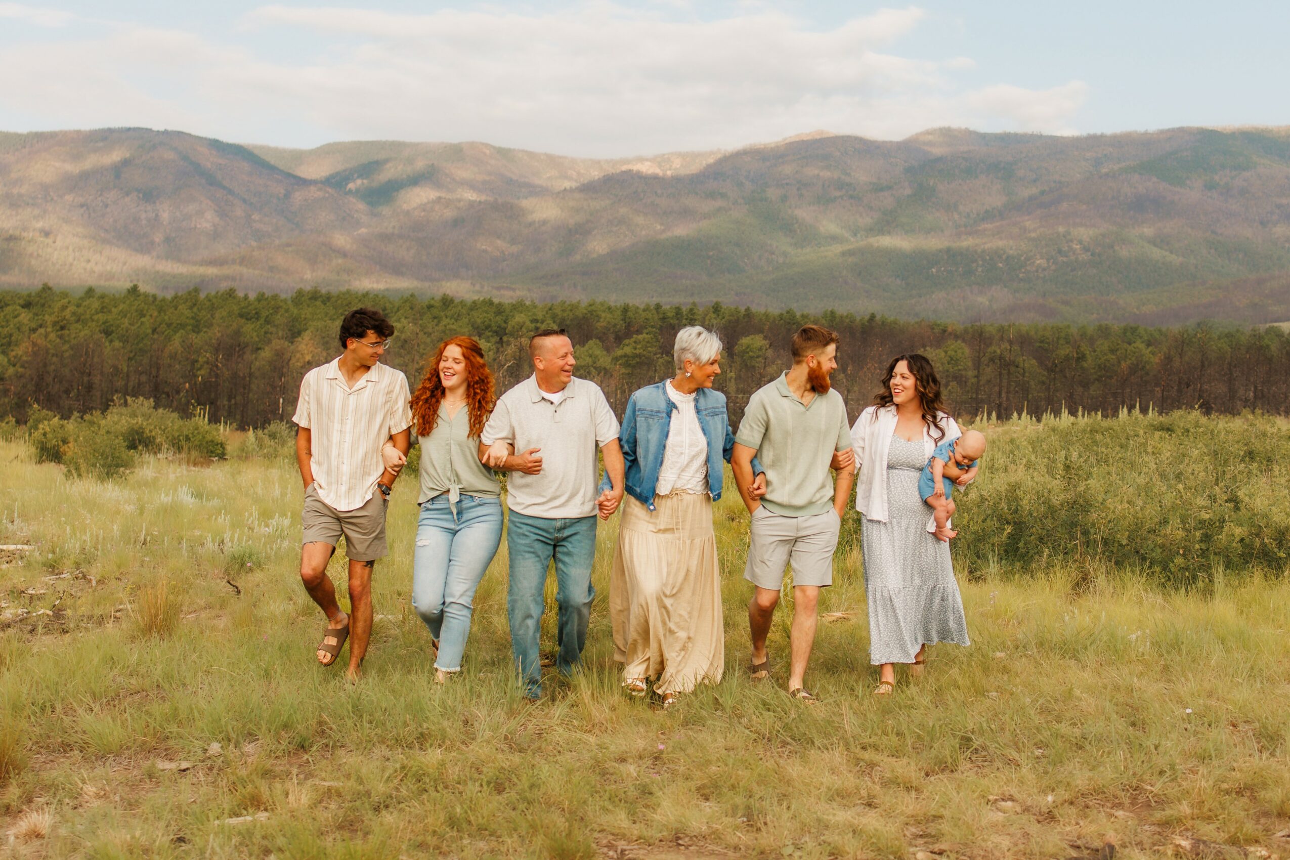 Group of seven people walking in a grassy field with mountains in the background.