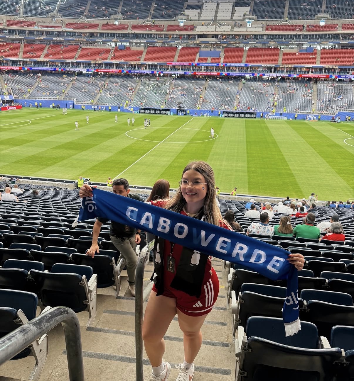 Young woman holding a blue scarf in a stadium with a green field and spectators.