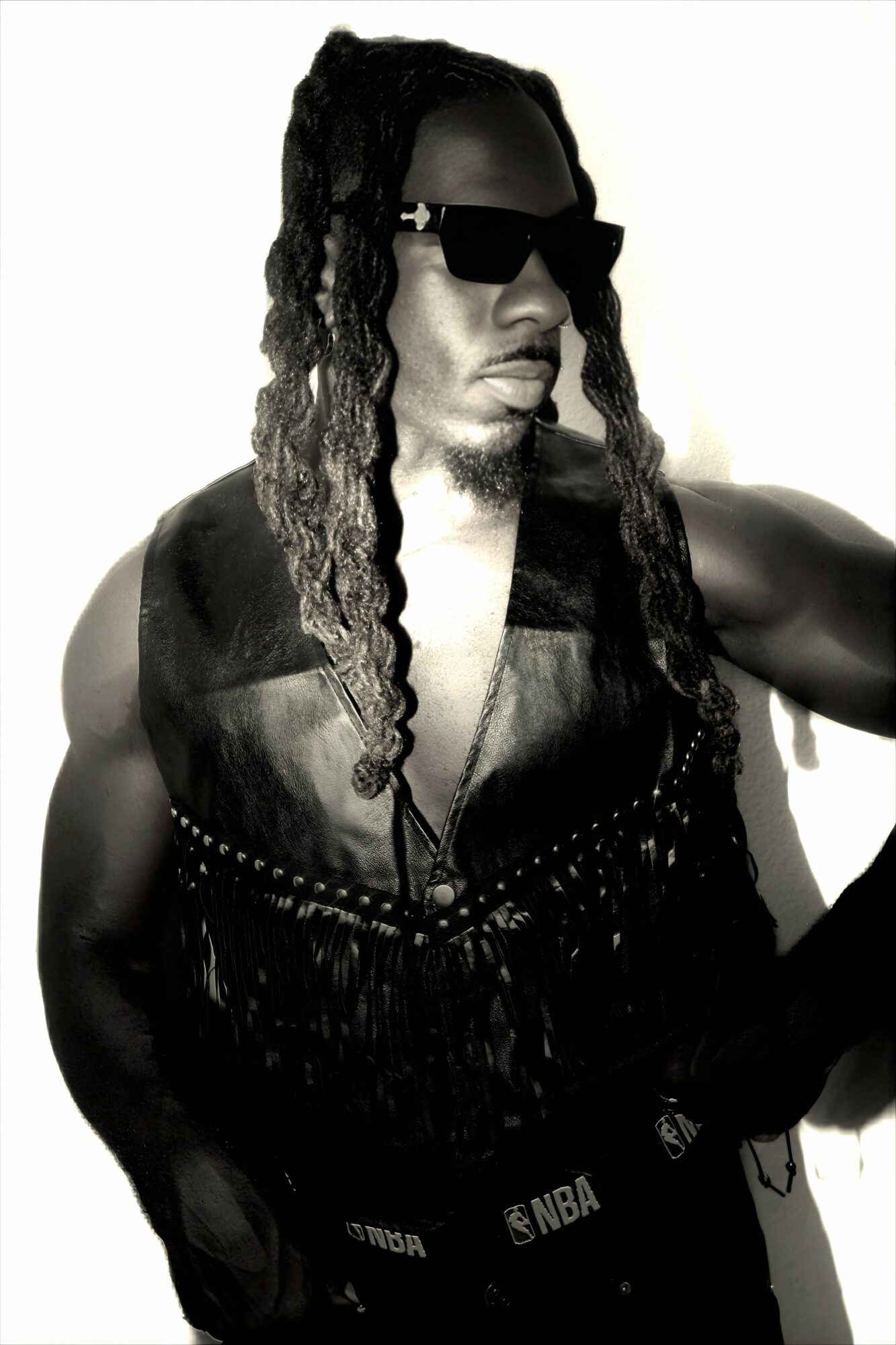 Person with long dreadlocks wearing sunglasses and a sleeveless top, posing against a light background.
