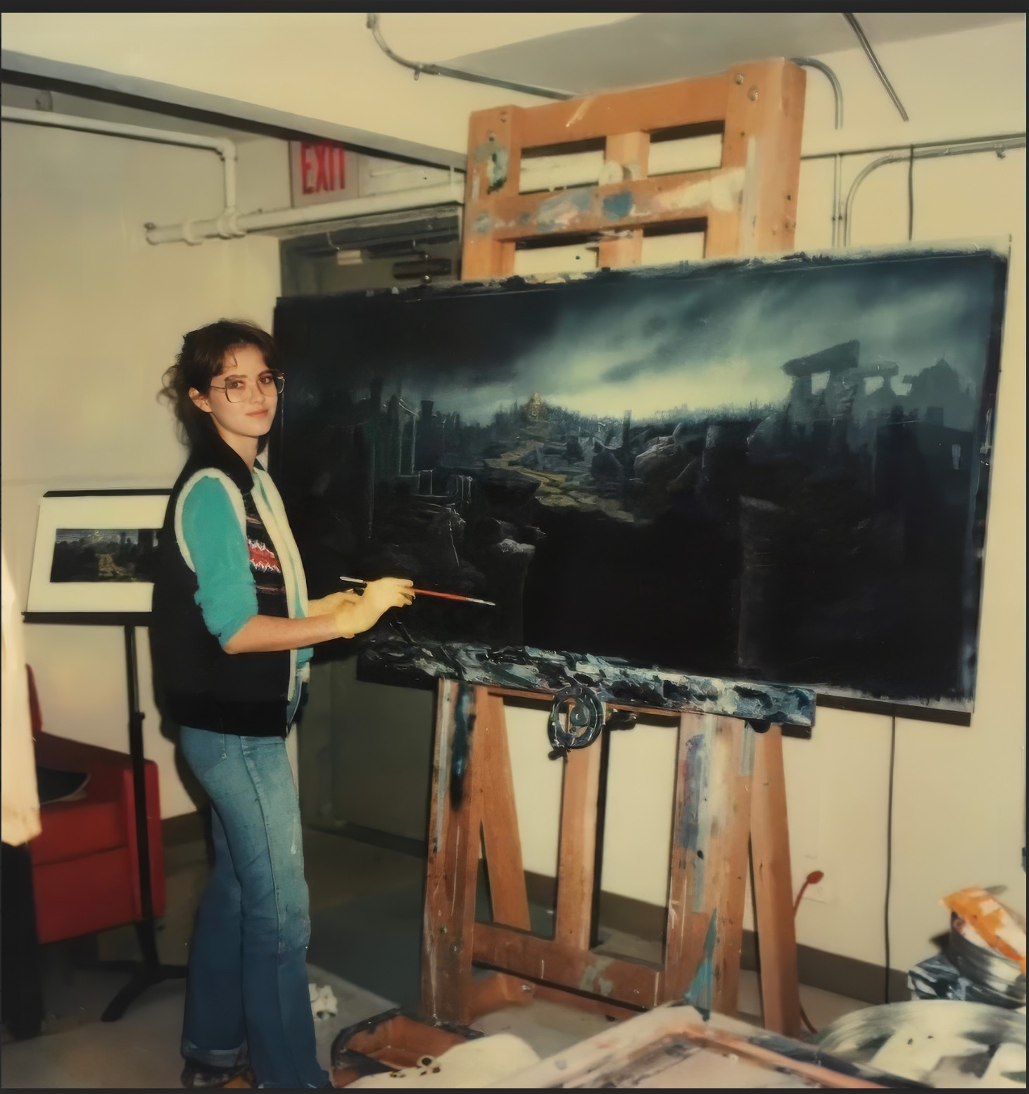 Young woman painting a landscape on a large canvas in an art studio, standing next to an easel and palette, with art supplies nearby.