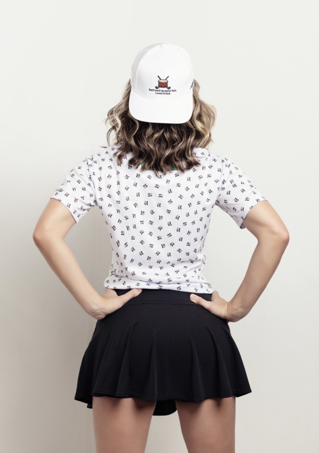 Person with curly hair wearing a white cap, polka dot shirt, and black skirt, facing away from the camera.