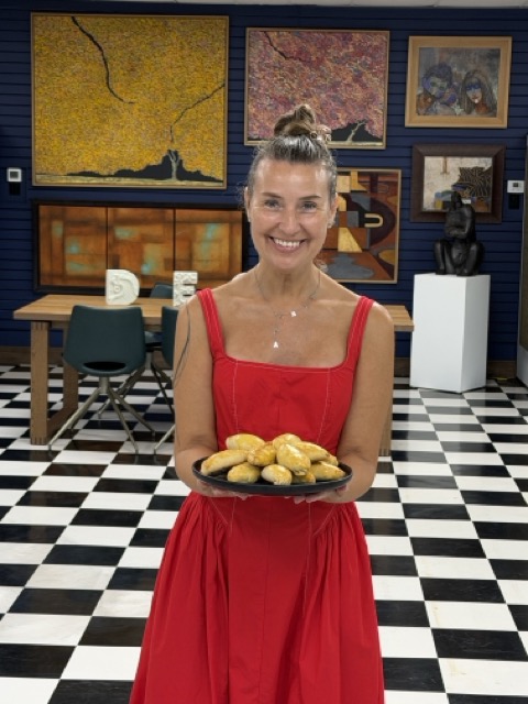 Smiling woman in red dress holding a plate of cookies in an art gallery with paintings and checkered floor.