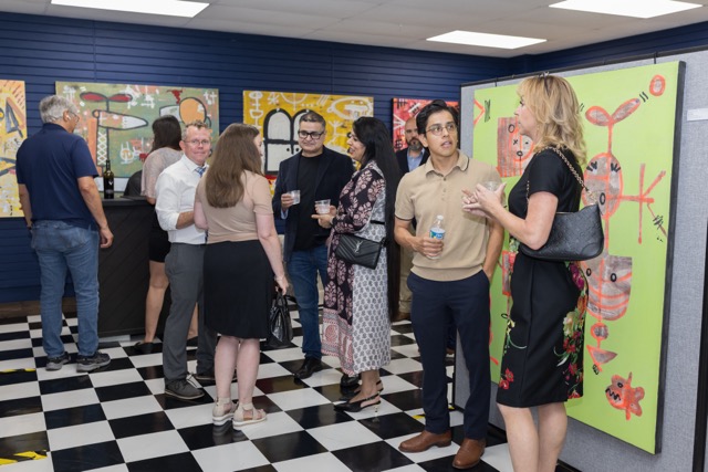 Group of people talking and interacting in an indoor space with colorful artwork on the walls and a checkered floor.