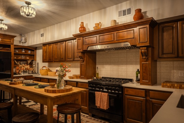 Kitchen with wooden cabinets, a stove, a dining table with a vase of flowers, and decorative items on top of cabinets.