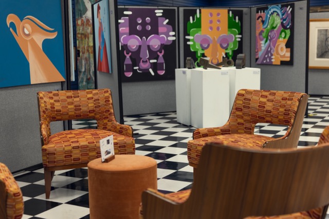 Three chairs and a small round table in an art gallery with colorful paintings on the wall.
