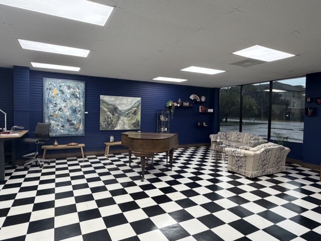 Room with checkered black and white floor, blue walls, large window, piano, artwork, and seating area.