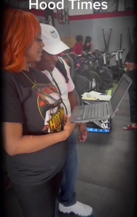 Woman with orange hair looking at a laptop in a store, with people and bikes in the background.