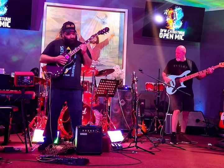 Two musicians perform on stage with guitars, surrounded by musical equipment and colorful lighting.