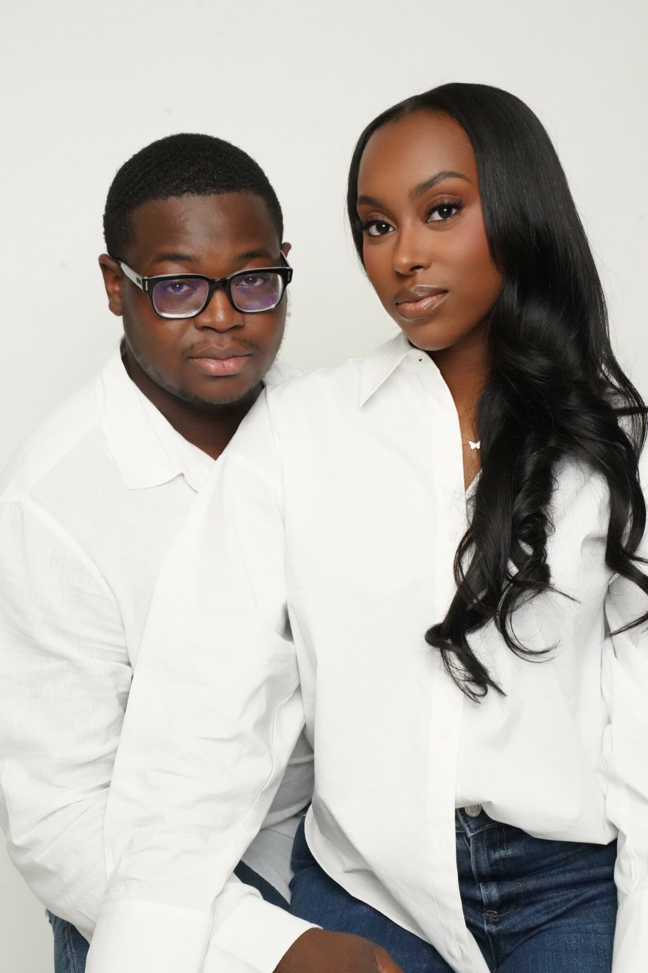 A man and woman pose together, both wearing white shirts, against a plain background.