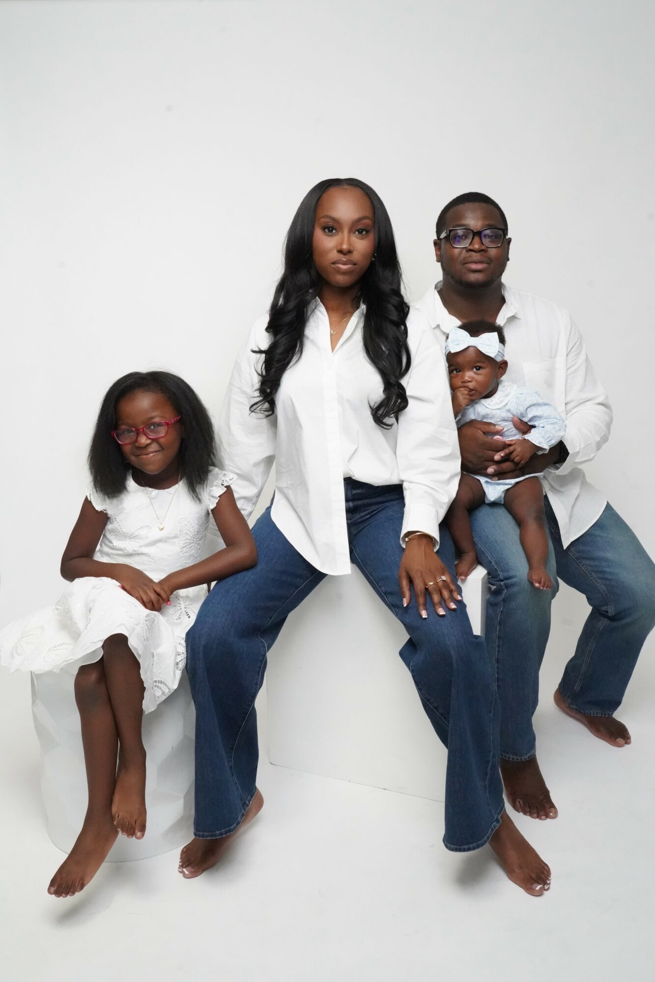 Family of four sitting against a white background, including two women and two children, all dressed in white and blue.