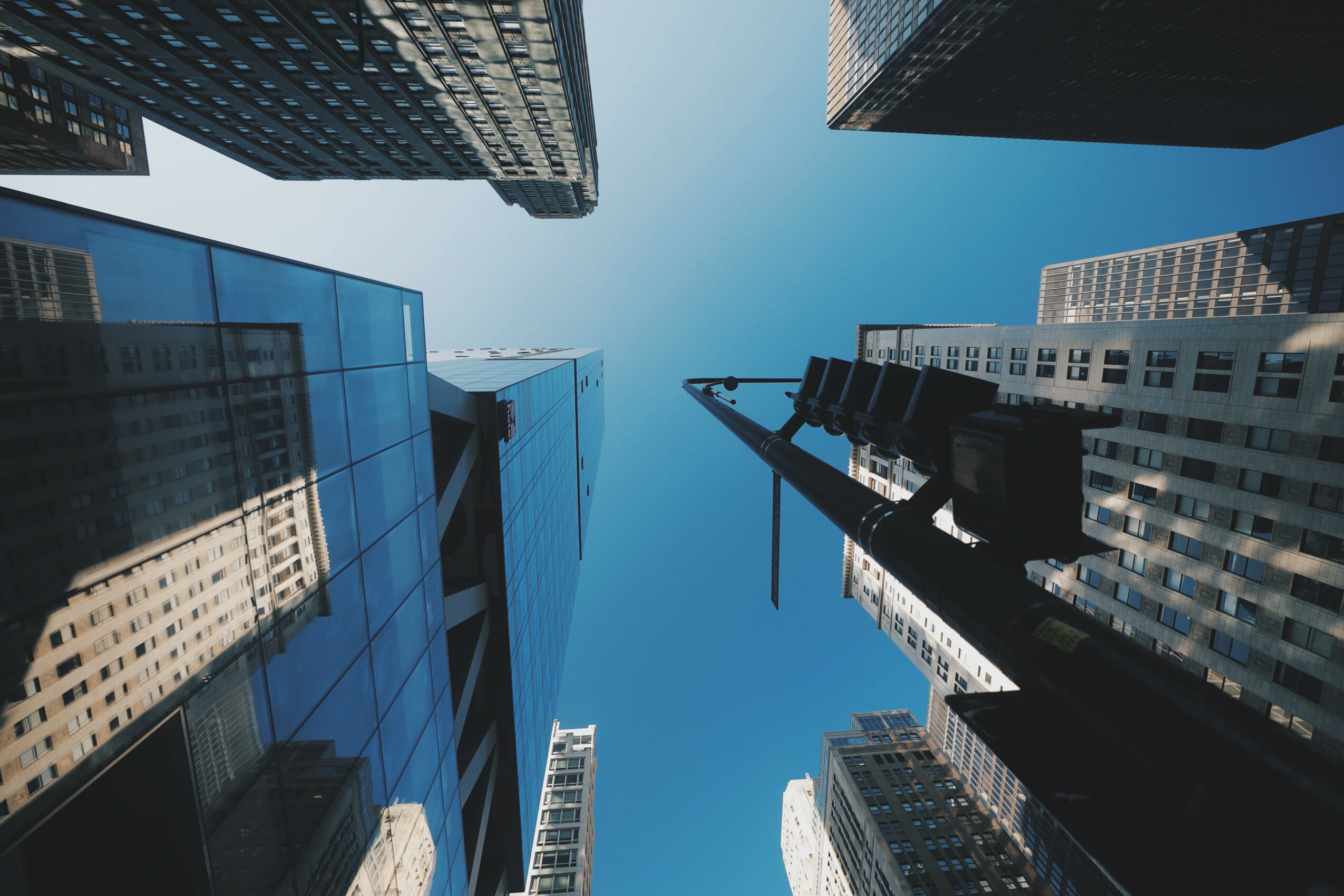 Looking up at tall skyscrapers against a clear blue sky from street level.