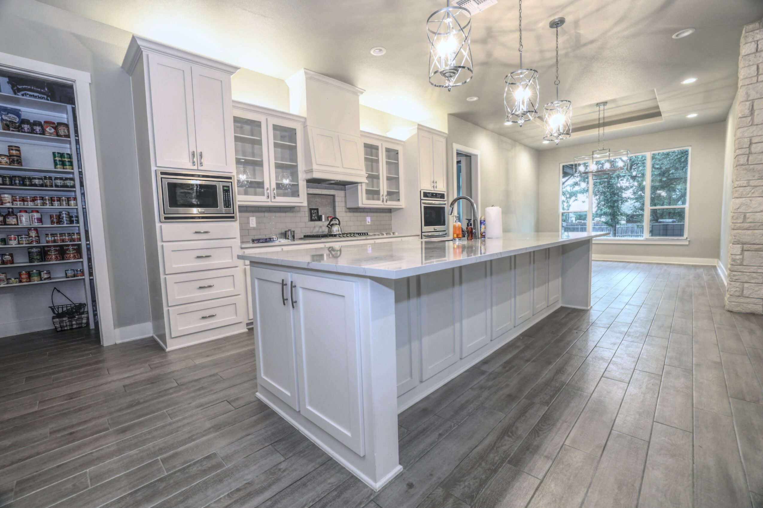 Modern kitchen with white cabinets, large island, and pendant lights, open to a bright living area with large windows.