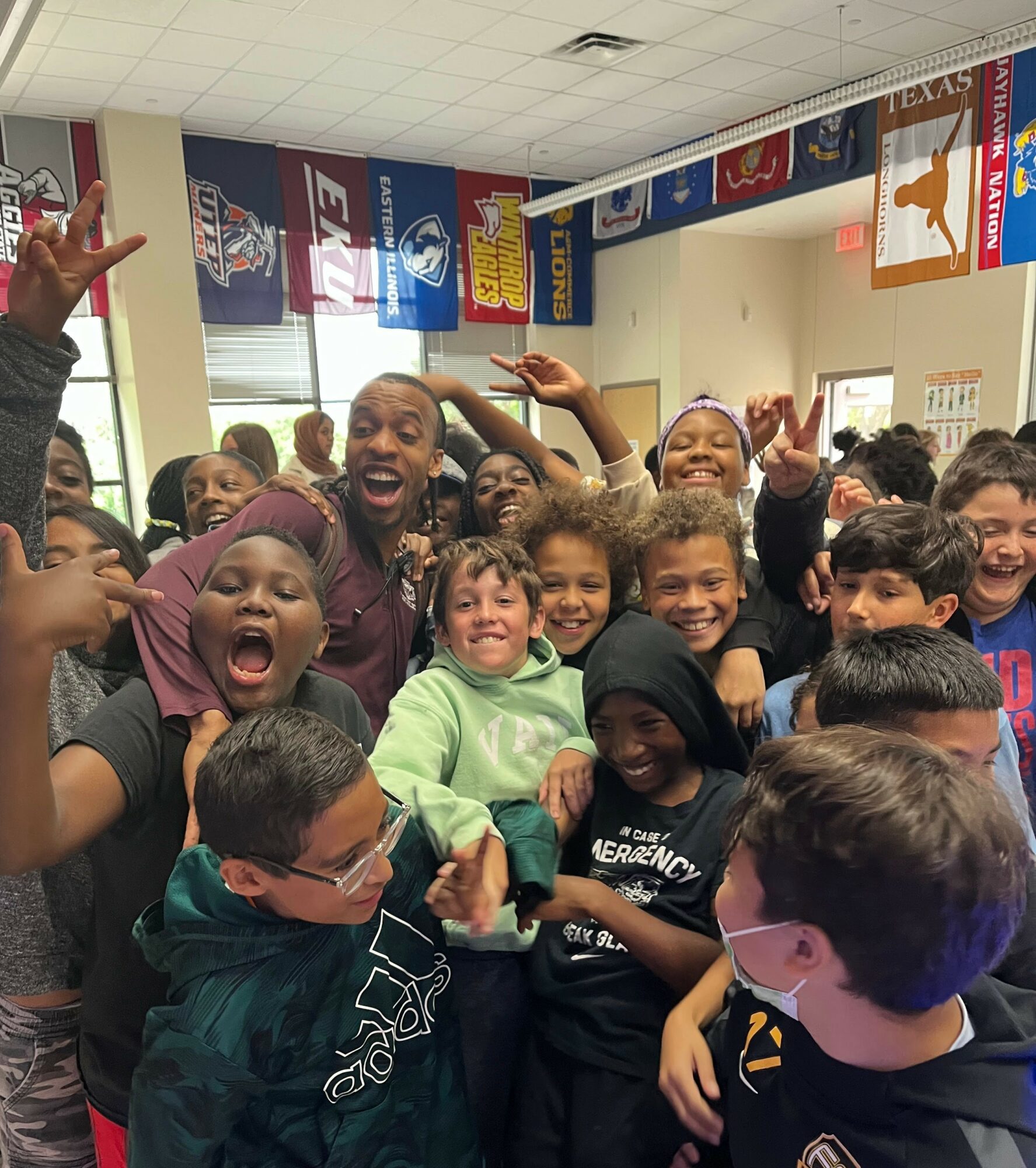 Group of children and adults smiling and celebrating in a classroom with banners hanging from the ceiling.
