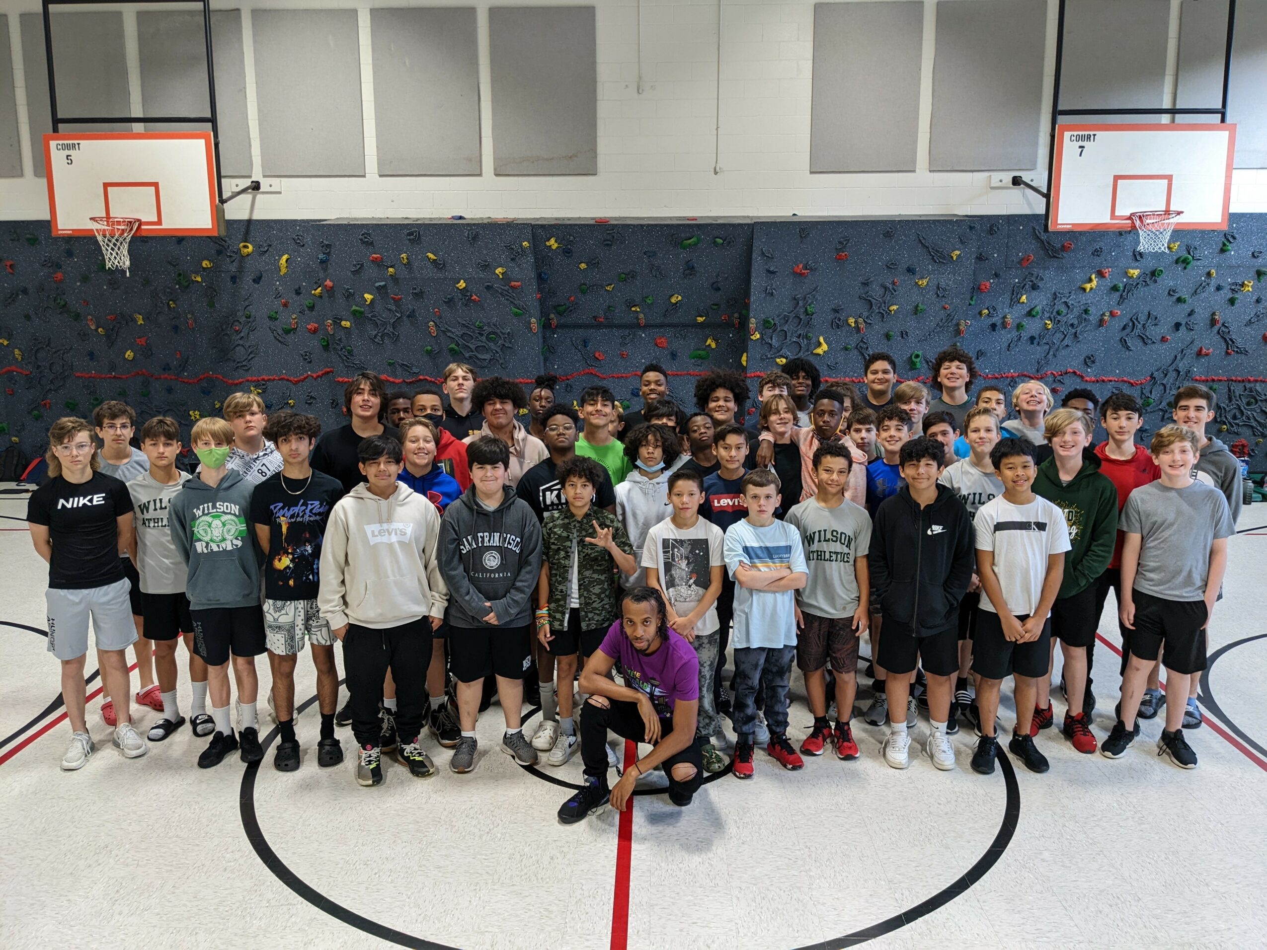 Group of children and teenagers in a gymnasium with basketball hoops, standing on a court with a red line, posing for a photo.