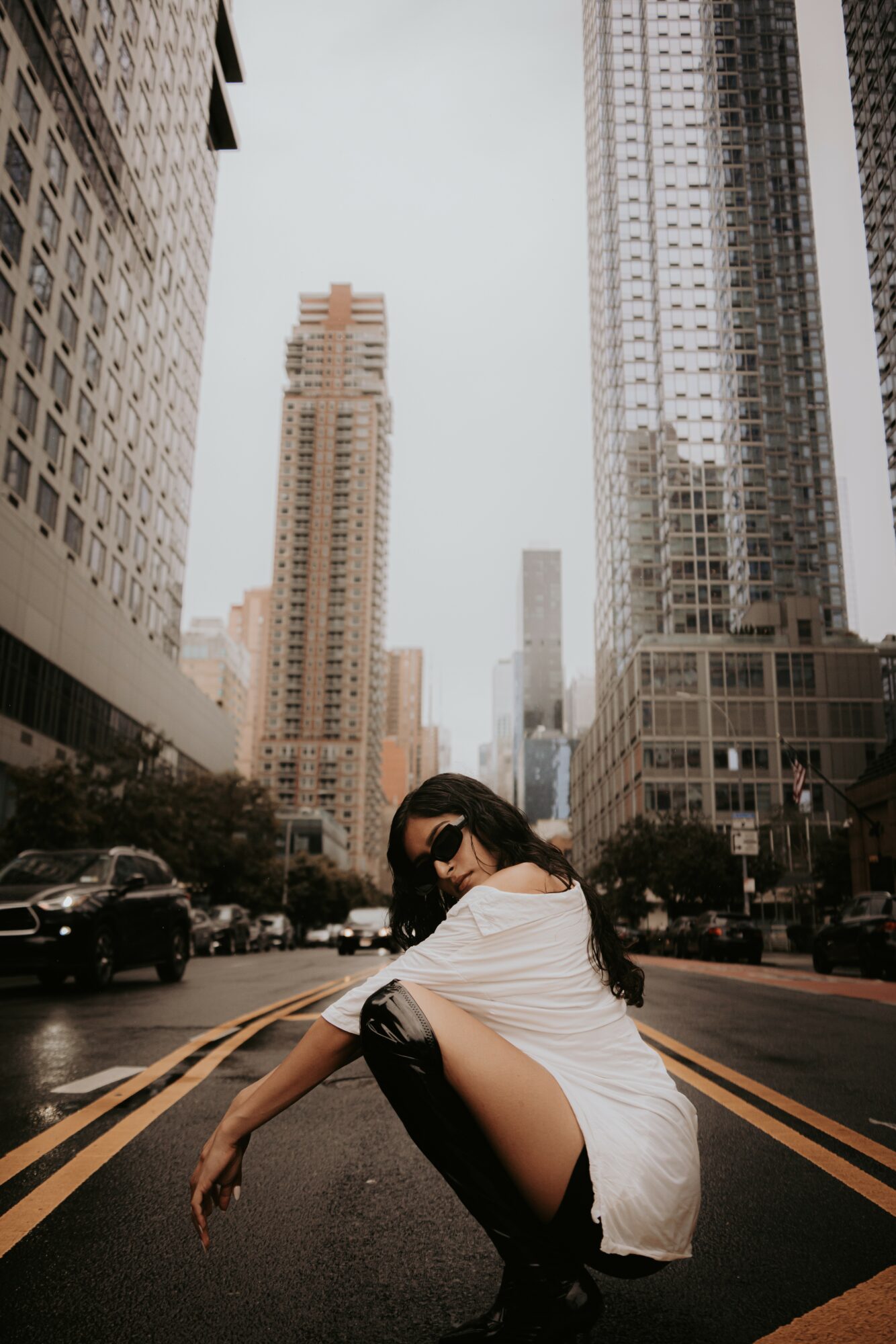 Woman crouching in the middle of a city street with tall skyscrapers around her.