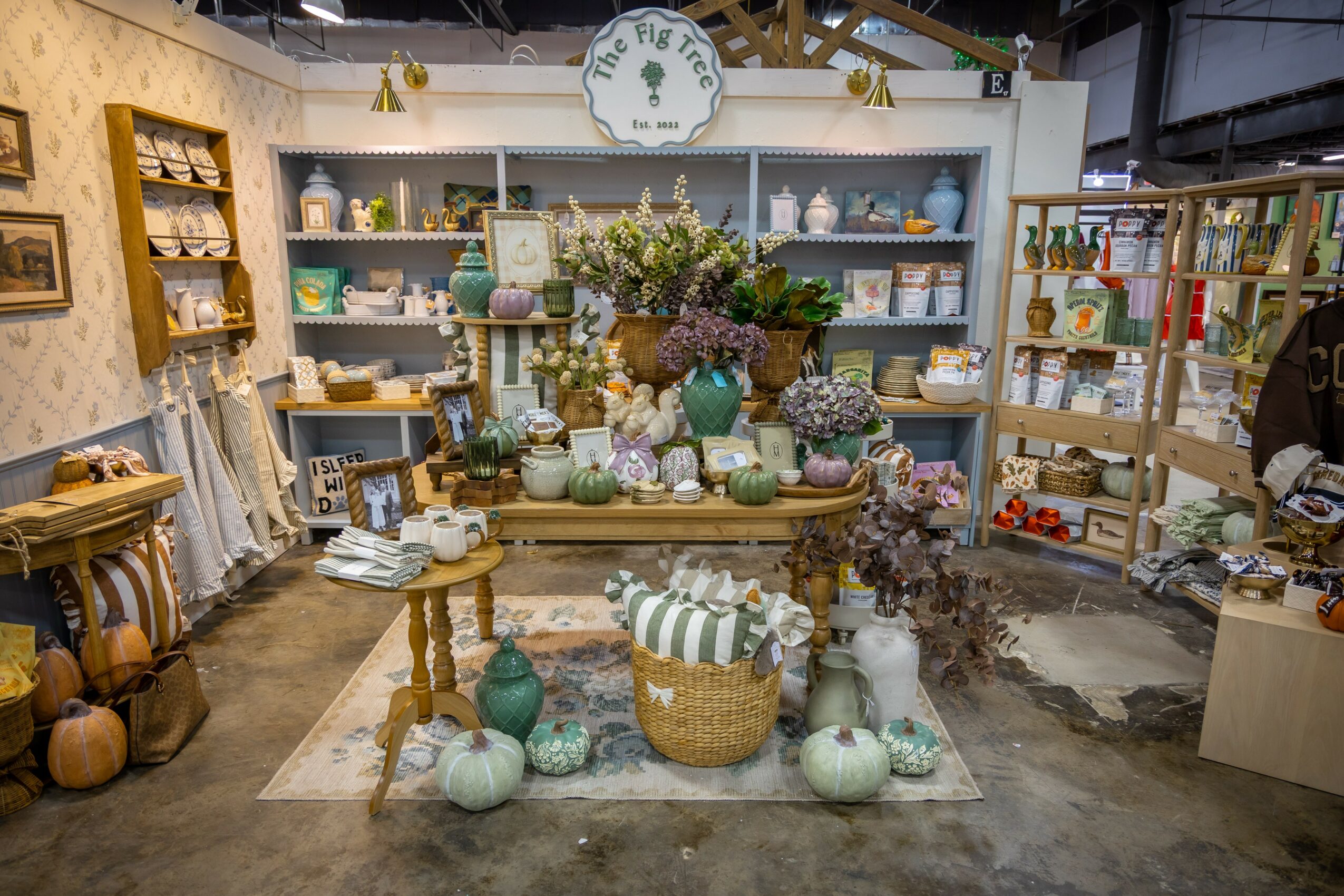 Display of ceramic vases, pumpkins, and flowers on shelves and table in a store, with decorative items and shelving units visible.