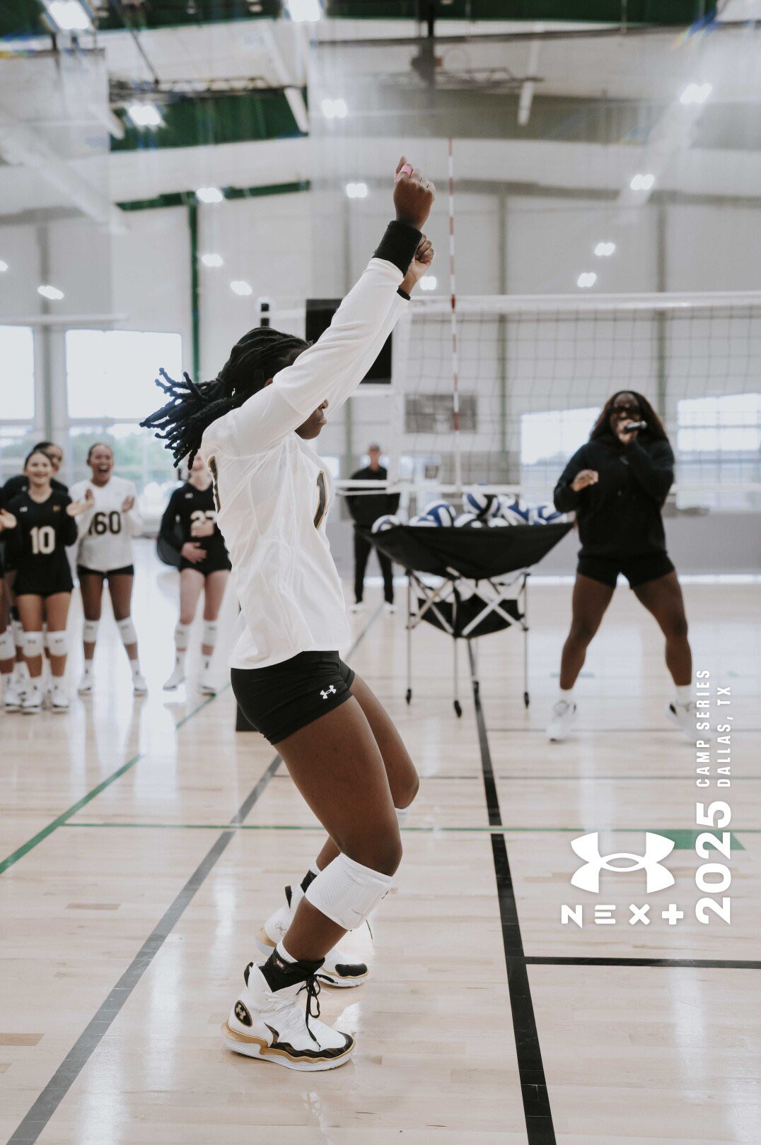 Person jumping with arms raised in an indoor volleyball court, with teammates and a coach in the background.