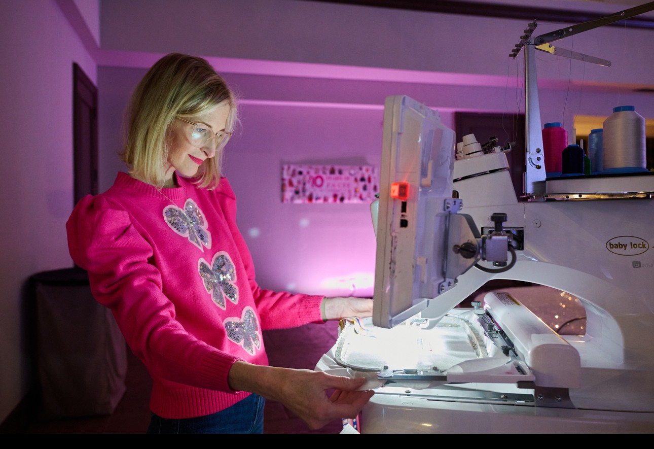 Woman in pink sweater with butterfly design working at a medical imaging machine in a clinical setting.