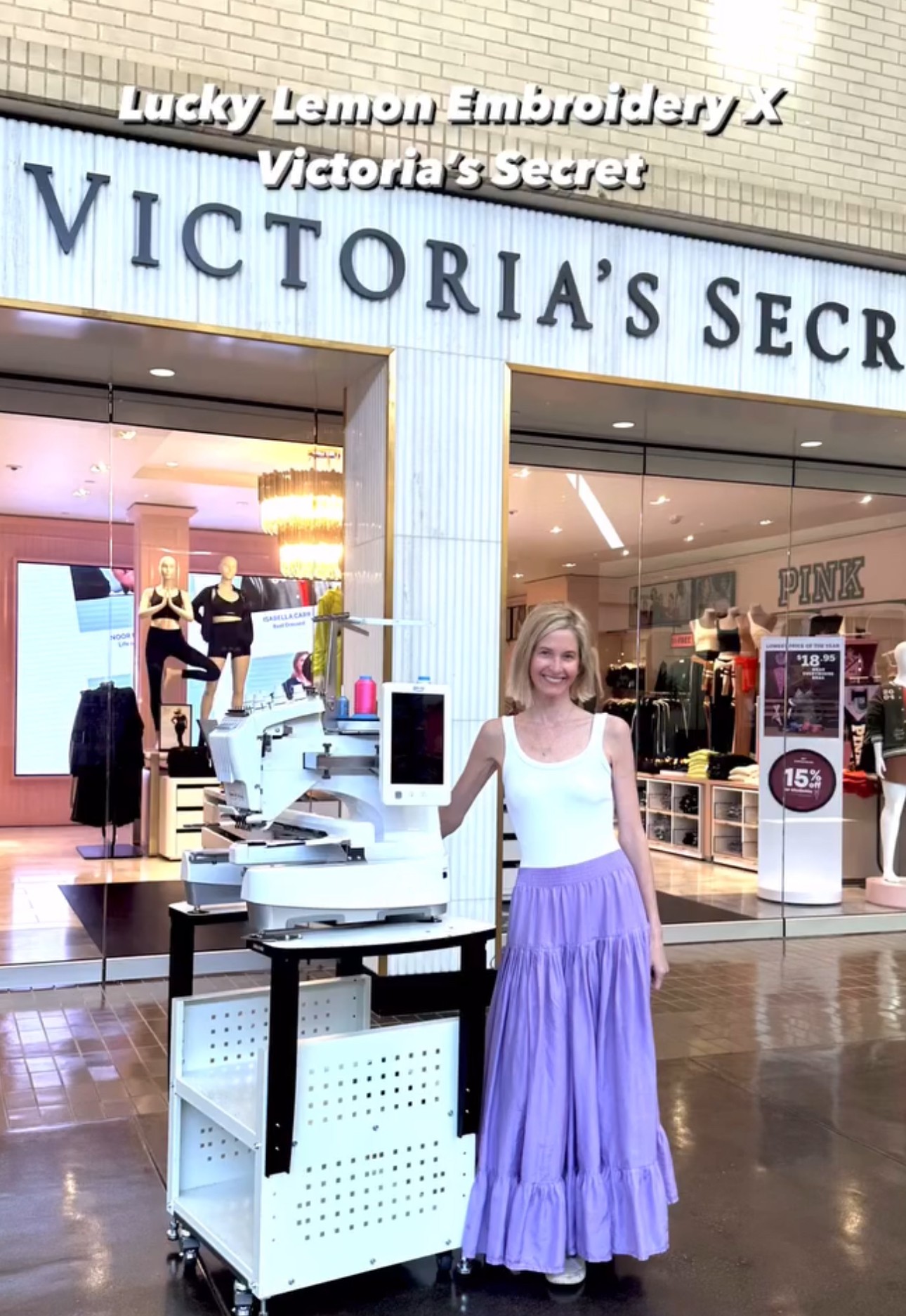 Young girl in a white top and purple skirt standing outside Victoria's Secret store, with store signage visible behind her.