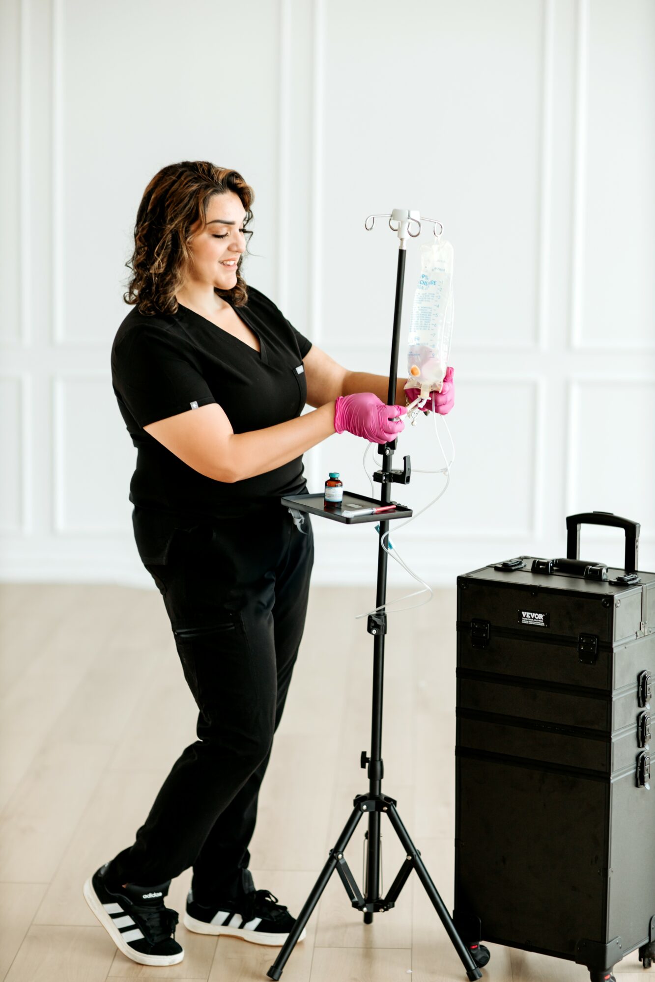 Woman in black clothes and pink gloves working with laboratory equipment in a bright room.