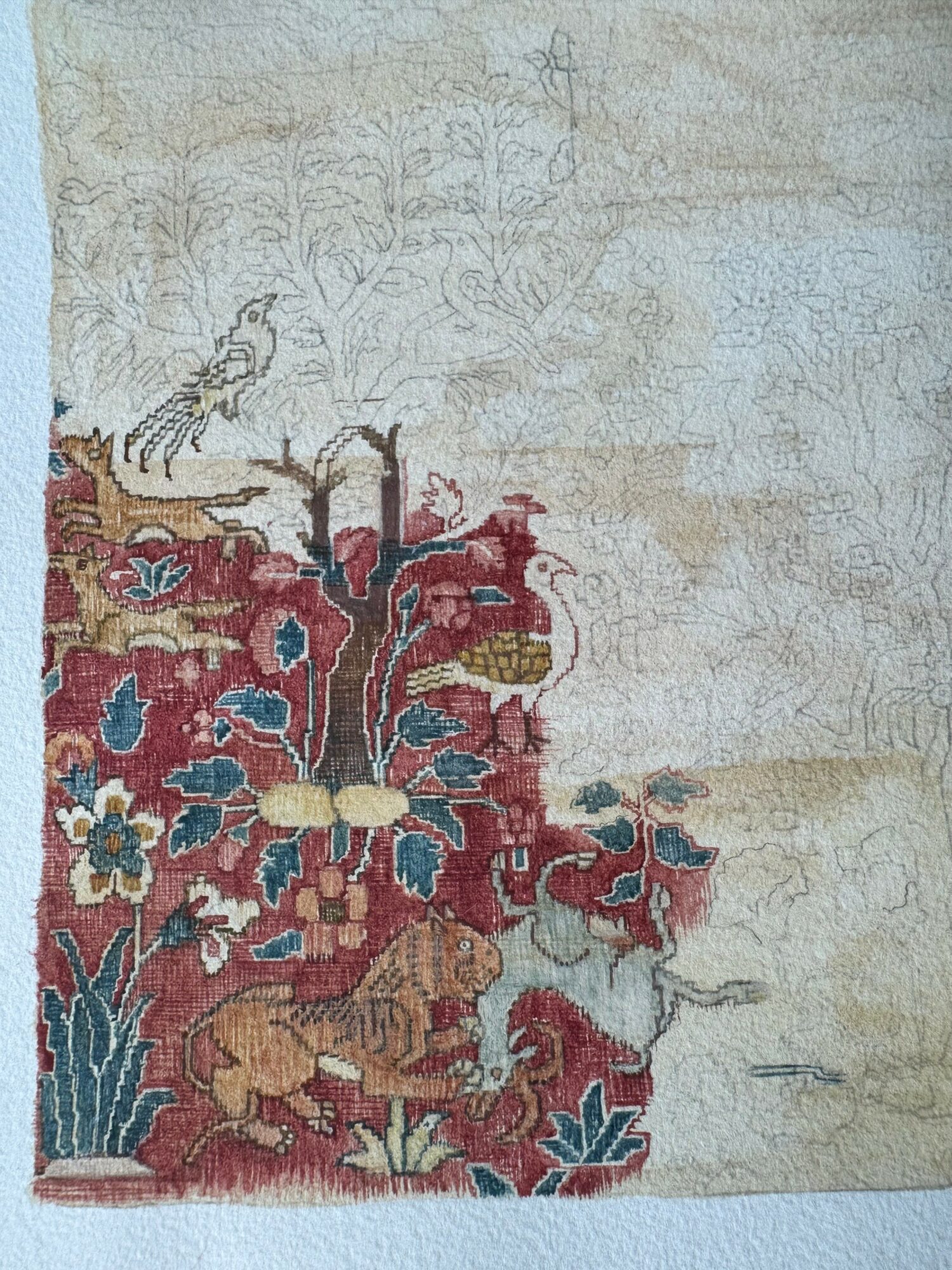 Part of a detailed textile or embroidery with animals and floral patterns, partially faded and worn.