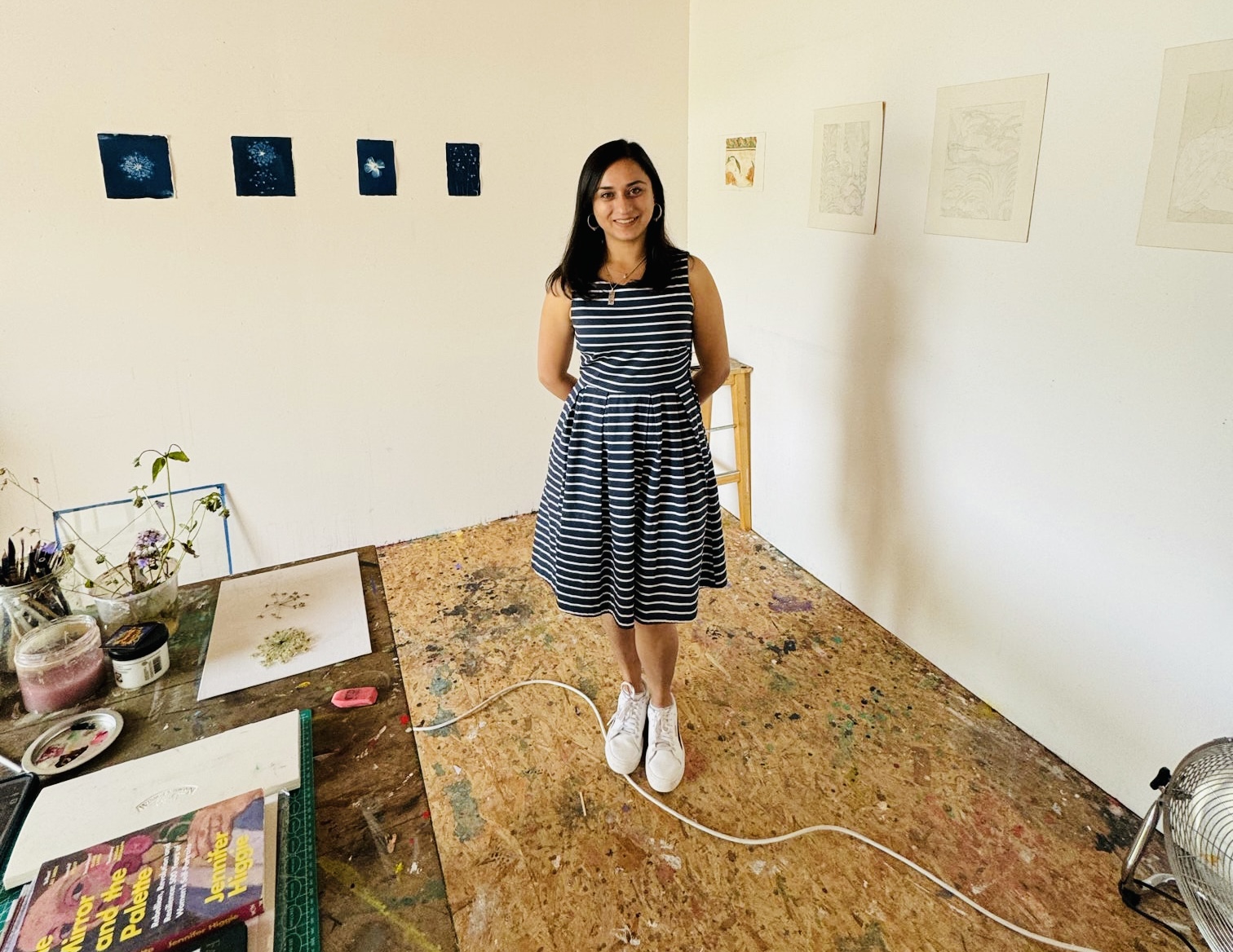 Young woman in a striped dress and white sneakers standing in an art gallery with artwork on white walls.
