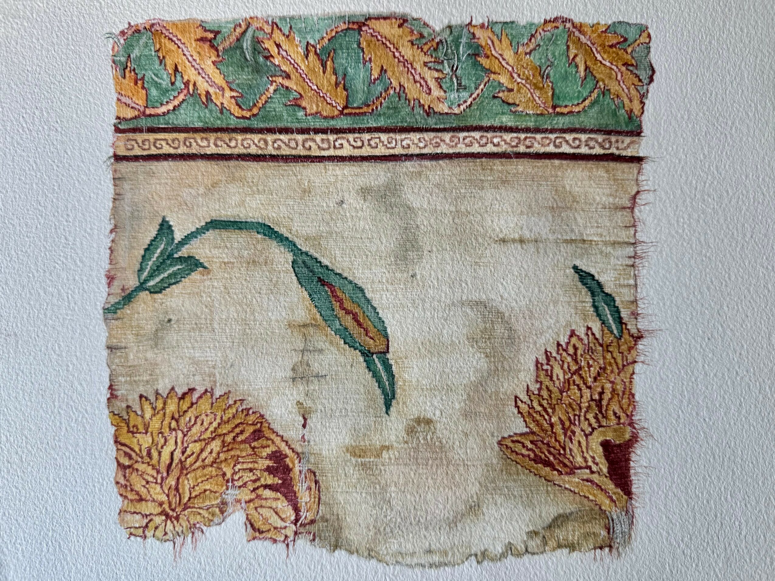 Fragment of a decorative textile with floral patterns and intricate borders, showing signs of wear and damage.