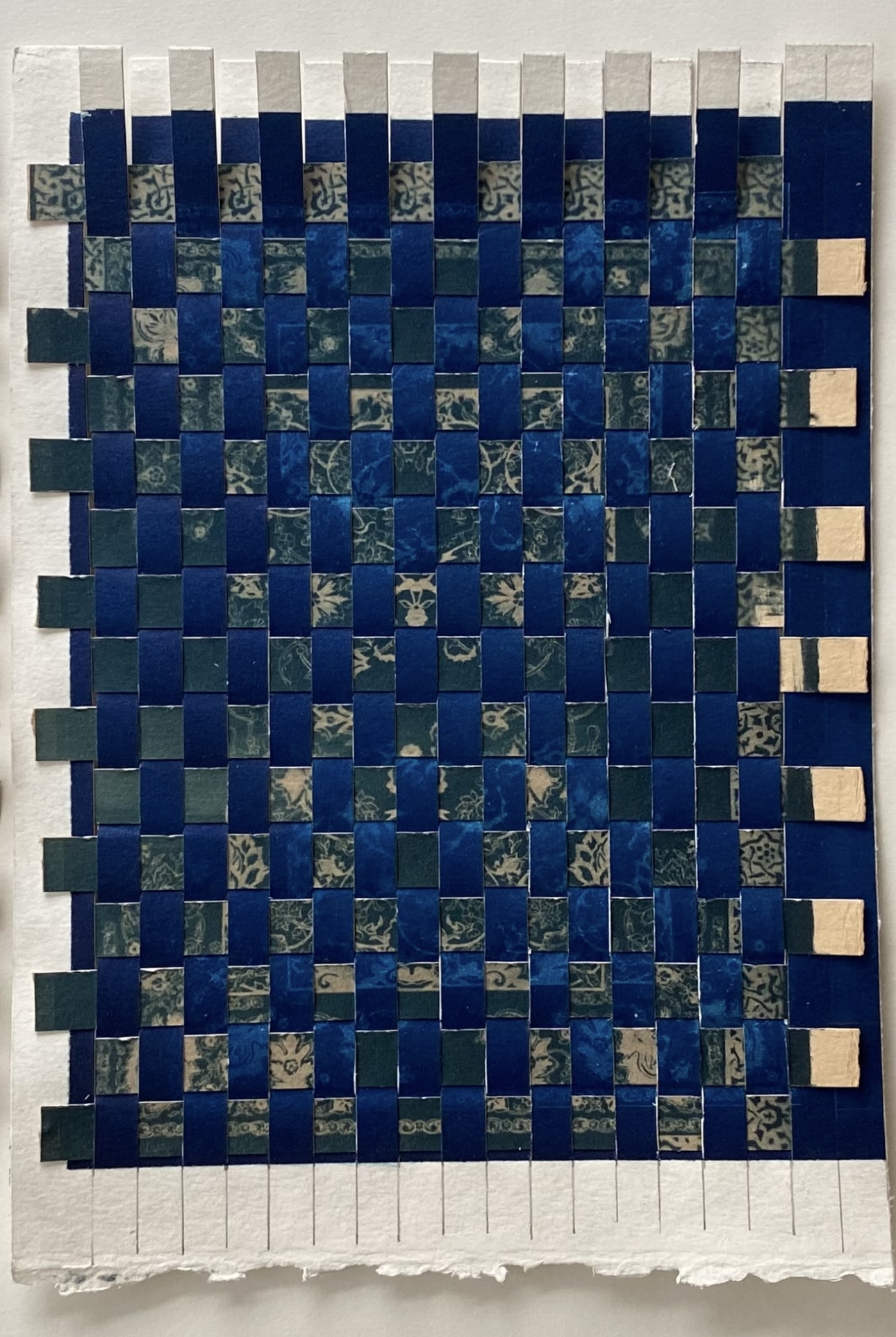 A woven mosaic of blue and beige tiles arranged in a checkered pattern, with a white border at the top and bottom.