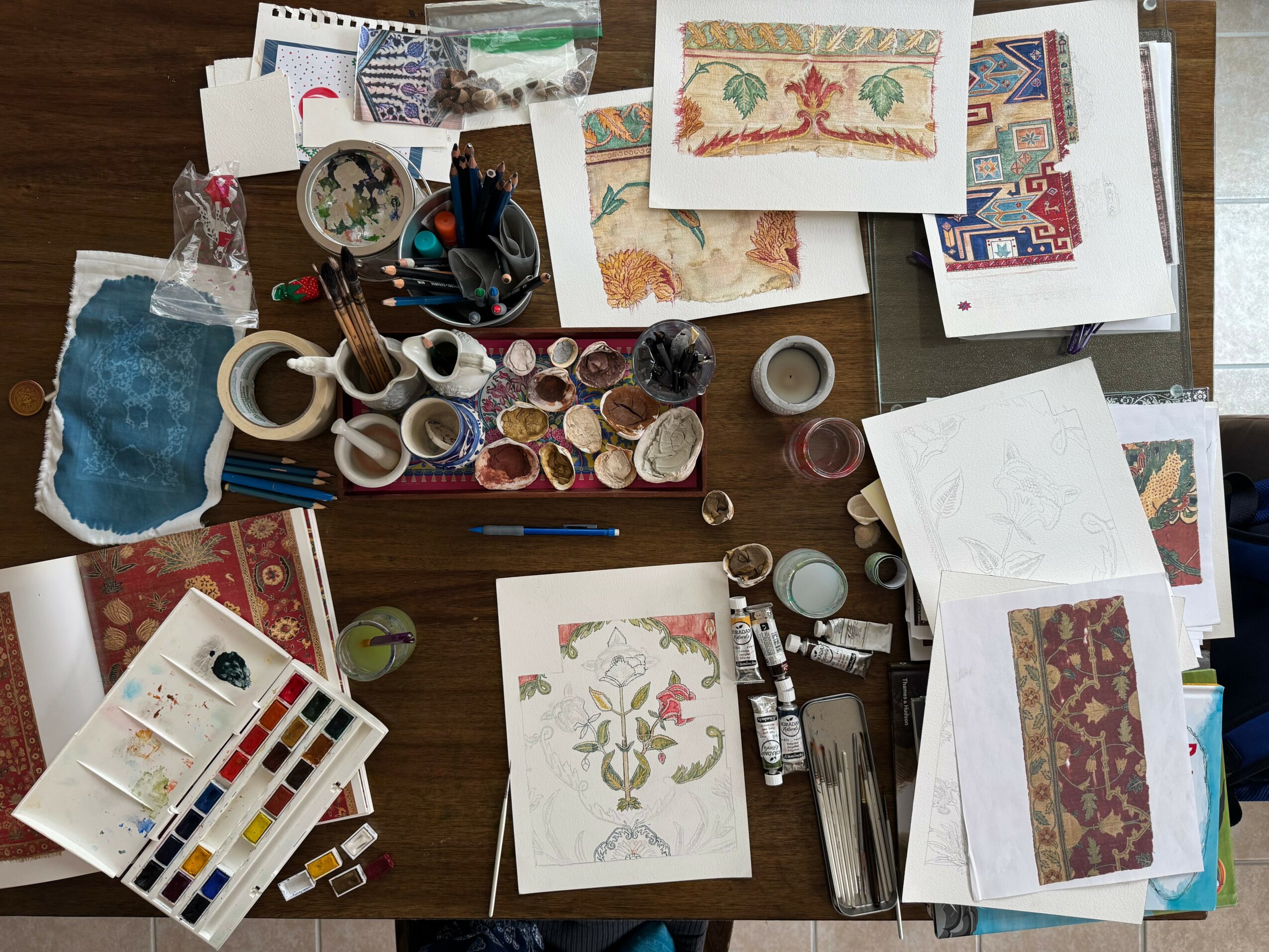 Art supplies, fabric pieces, and paper with embroidery and patterns on a wooden table.