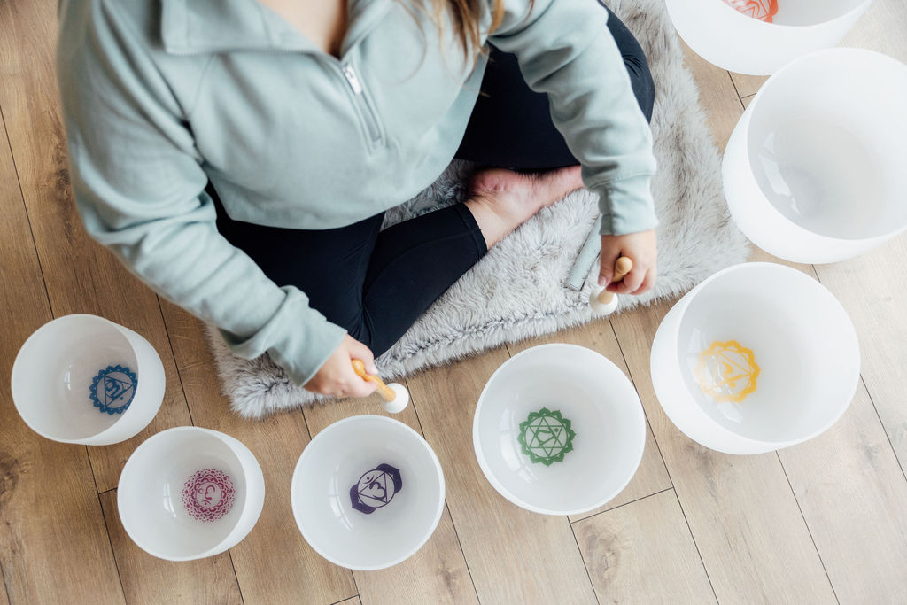 Person sitting cross-legged on a rug, surrounded by bowls with colorful patterns, on a wooden floor.