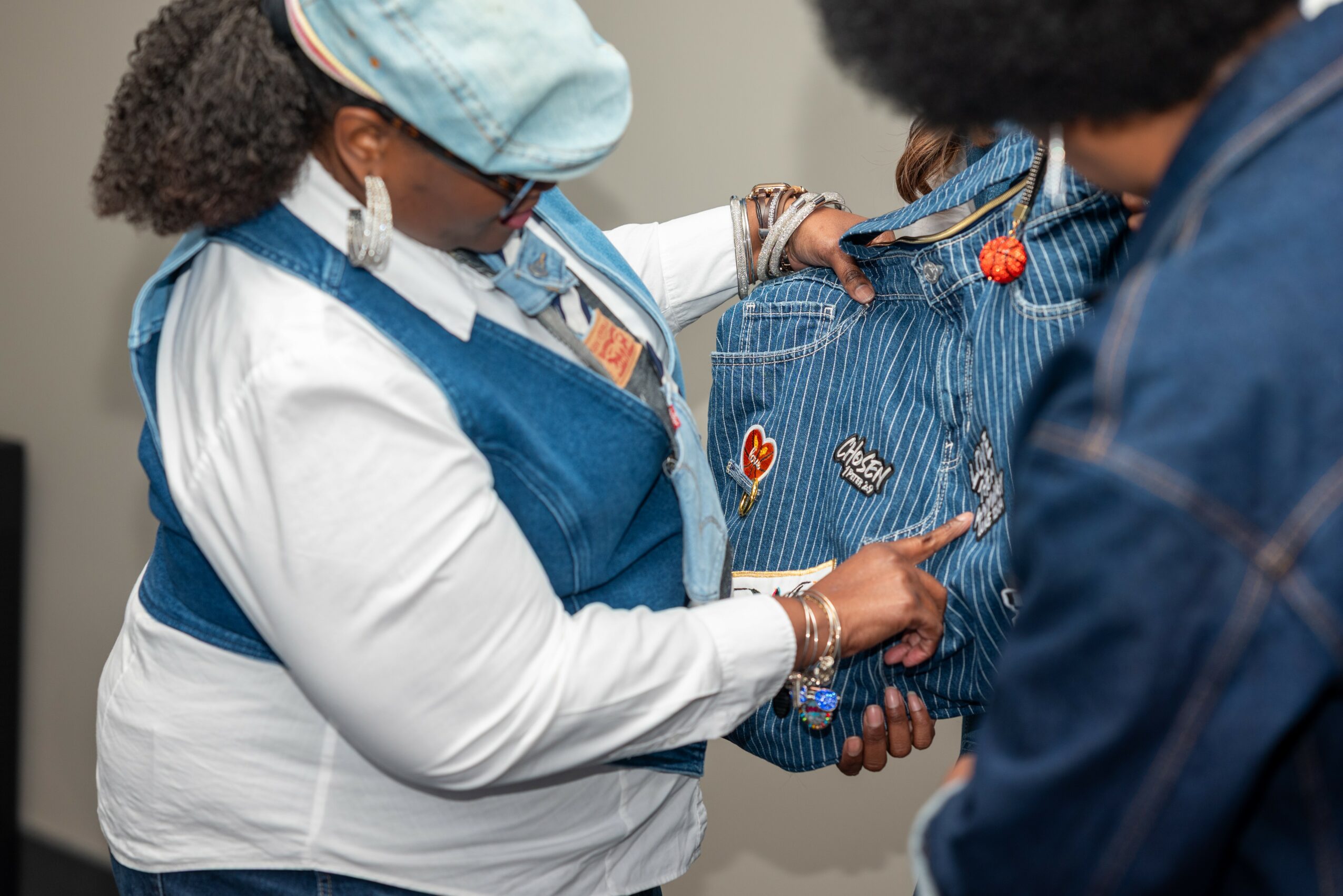 Two women exchange a blue striped bag with patches, one wearing a white shirt and blue apron, the other in a dark jacket.