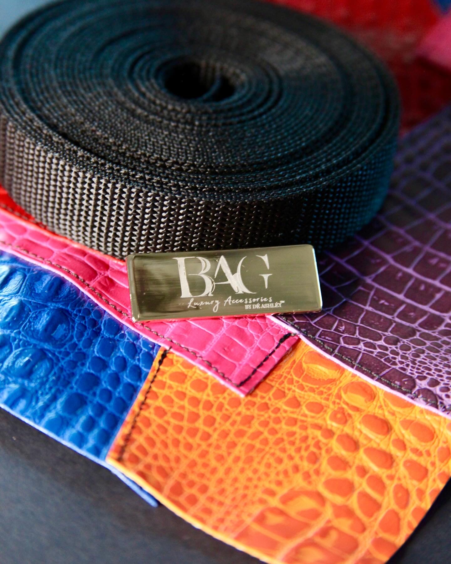 Coiled black strap with a metallic label reading 'BAG' on colorful textured fabric samples.