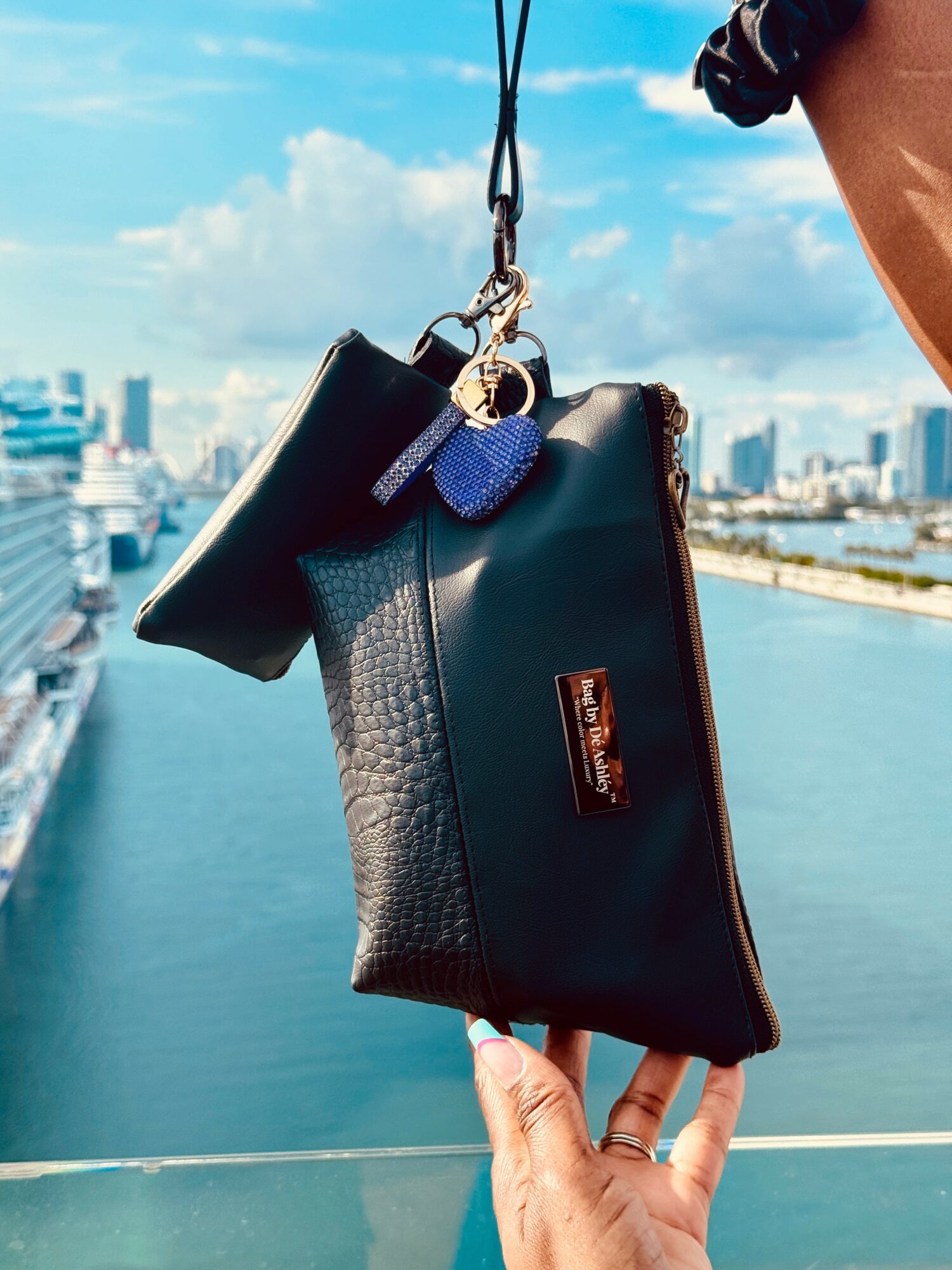 Person holding a black handbag with a blue keychain against a cityscape and river background.