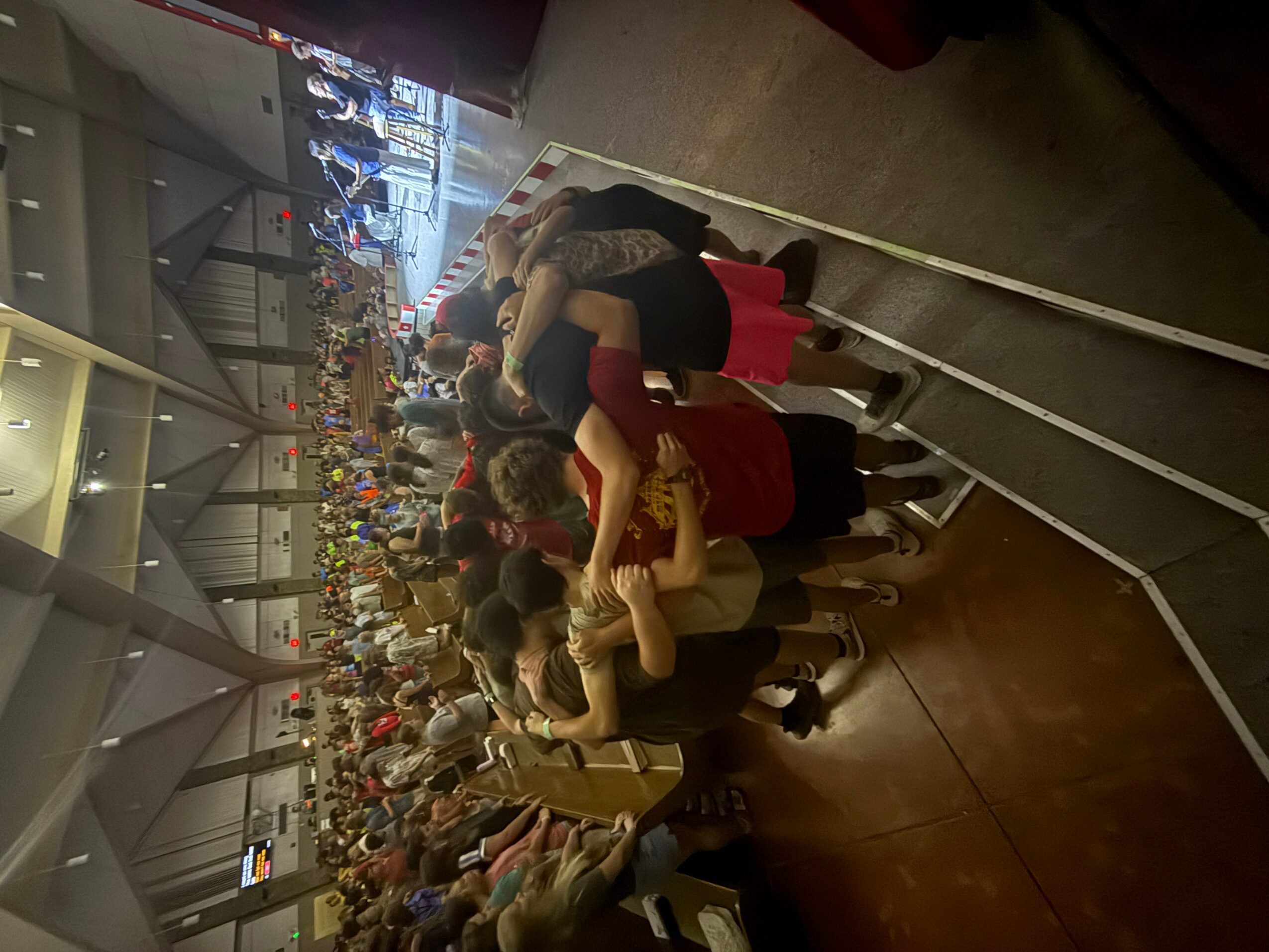 People seated in a row watching a large screen in a spacious indoor setting.