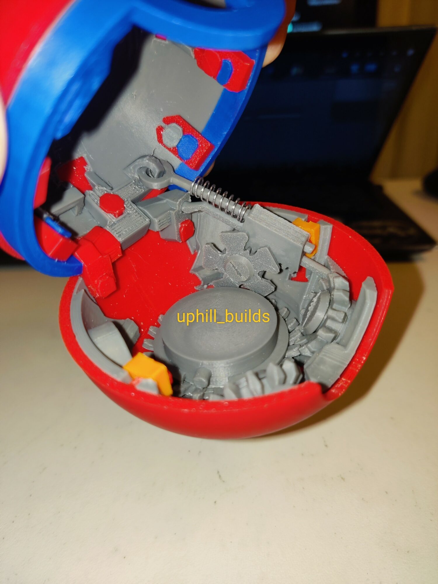Open red and blue plastic device with internal mechanical parts and a spring, placed on a white surface.