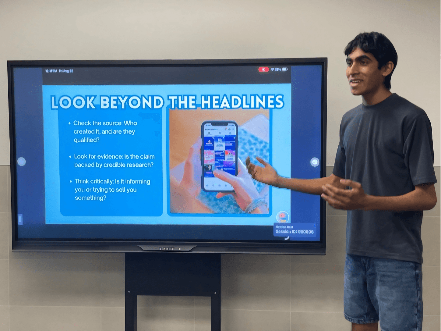 Person standing next to a screen displaying a presentation slide titled 'Look Beyond the Headlines' with bullet points and an image of a smartphone.