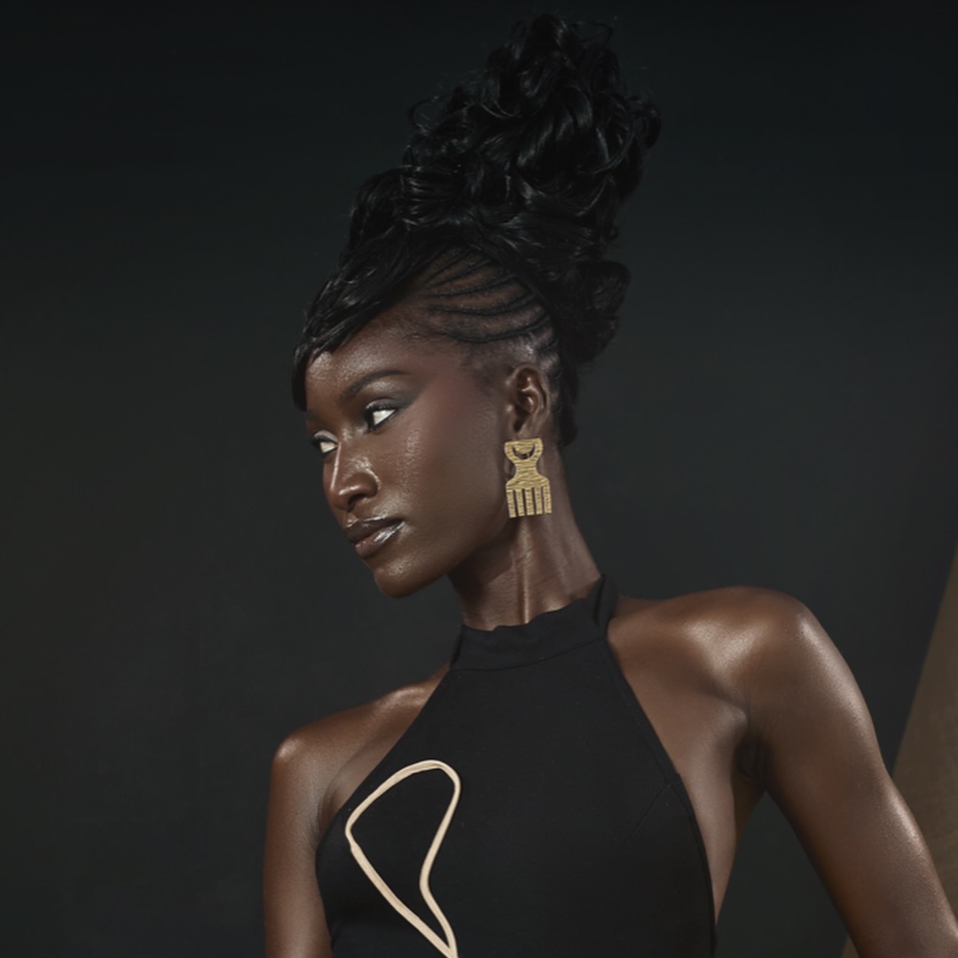 Portrait of a woman with styled hair, wearing a black halter top and gold earrings, against a dark background.