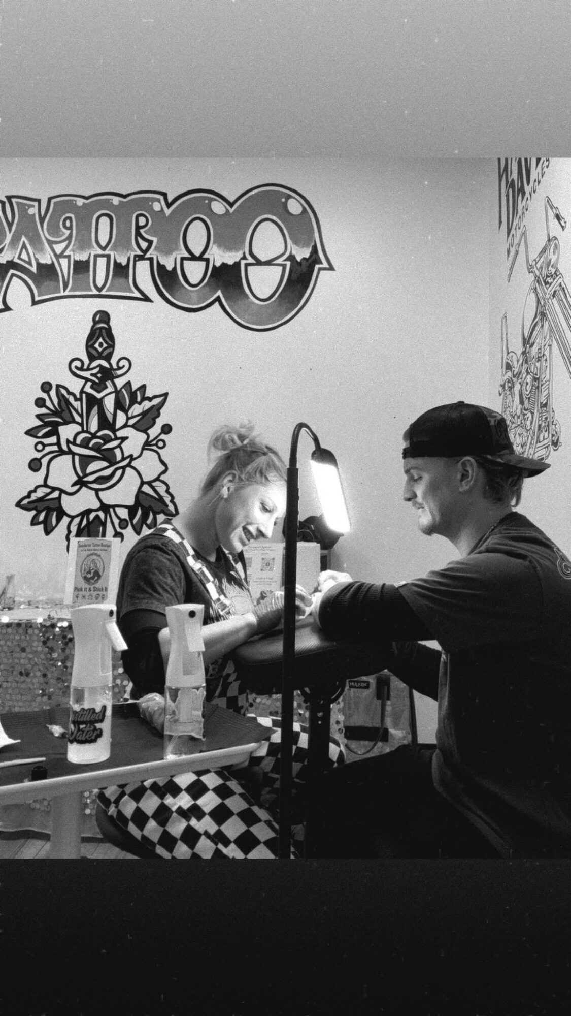 Two people sitting at a table, playing a game, with a lamp and wall art in the background.