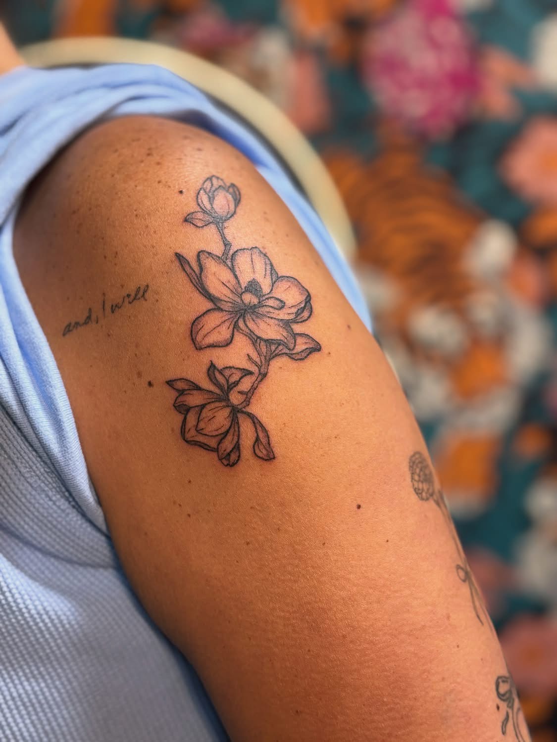 Tattoo of a flower with a stem and leaves on person's upper arm, with colorful background.