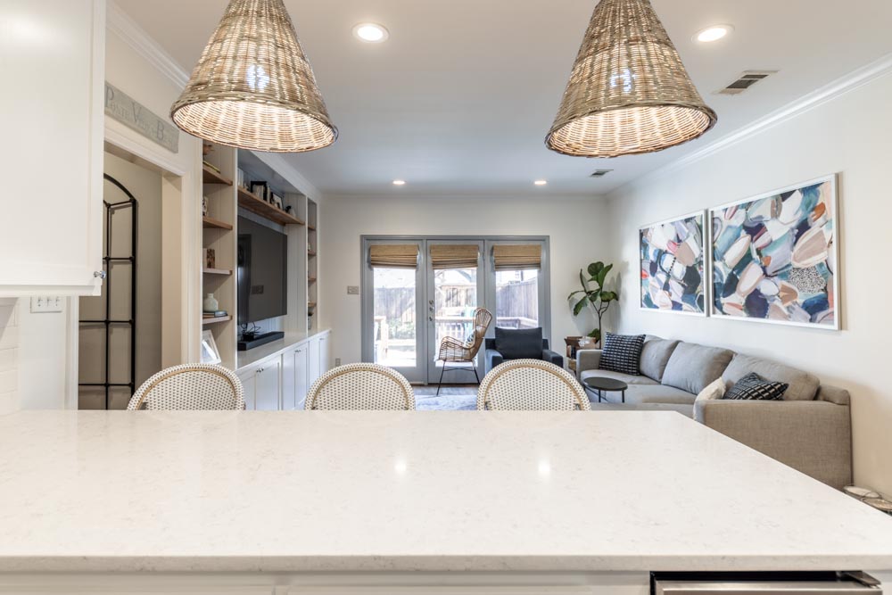 Living room with a sofa, artwork, and sliding glass doors leading outside, viewed from a white countertop.
