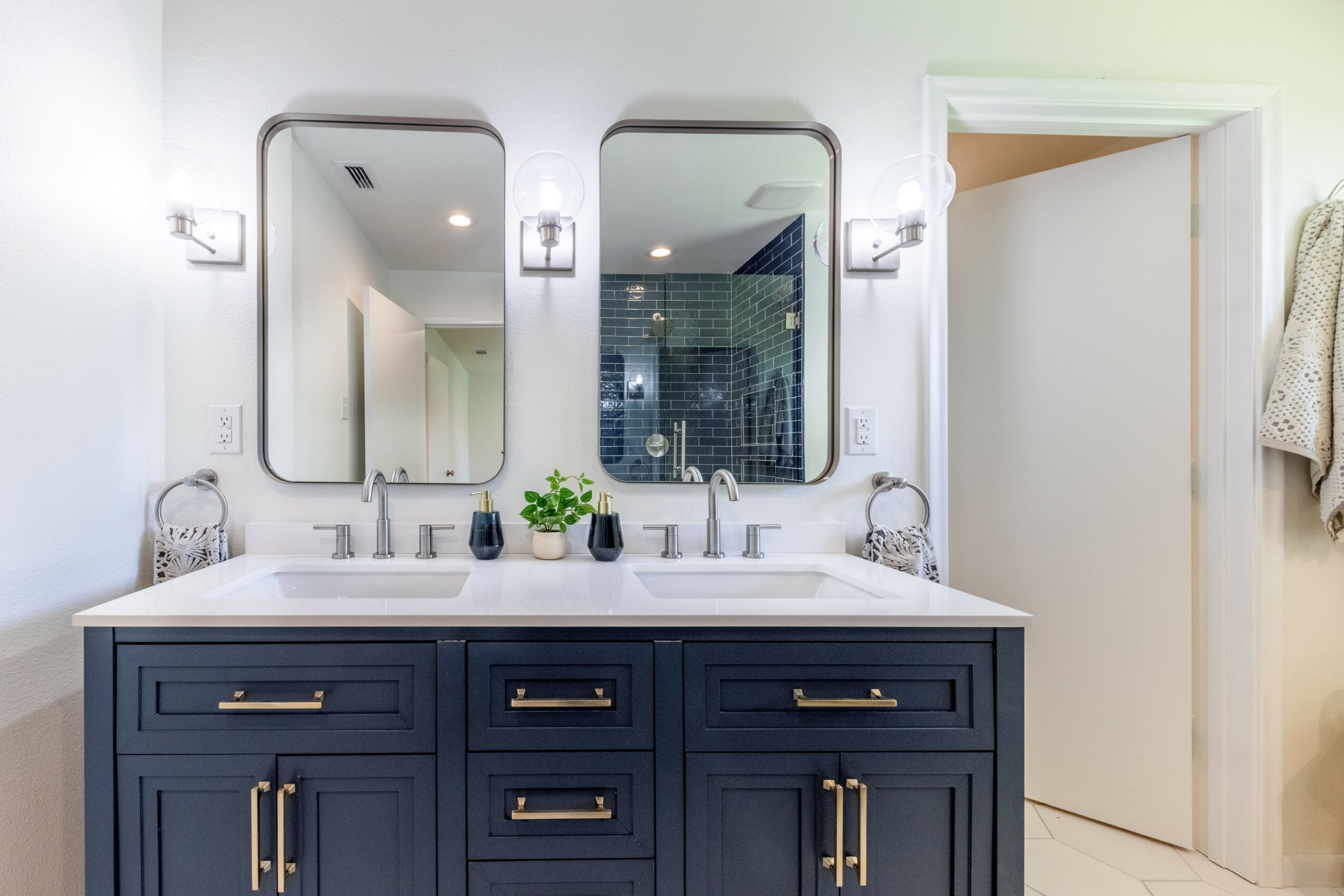 Double vanity with two mirrors, blue cabinet, two sinks, and wall-mounted lights in a bathroom.