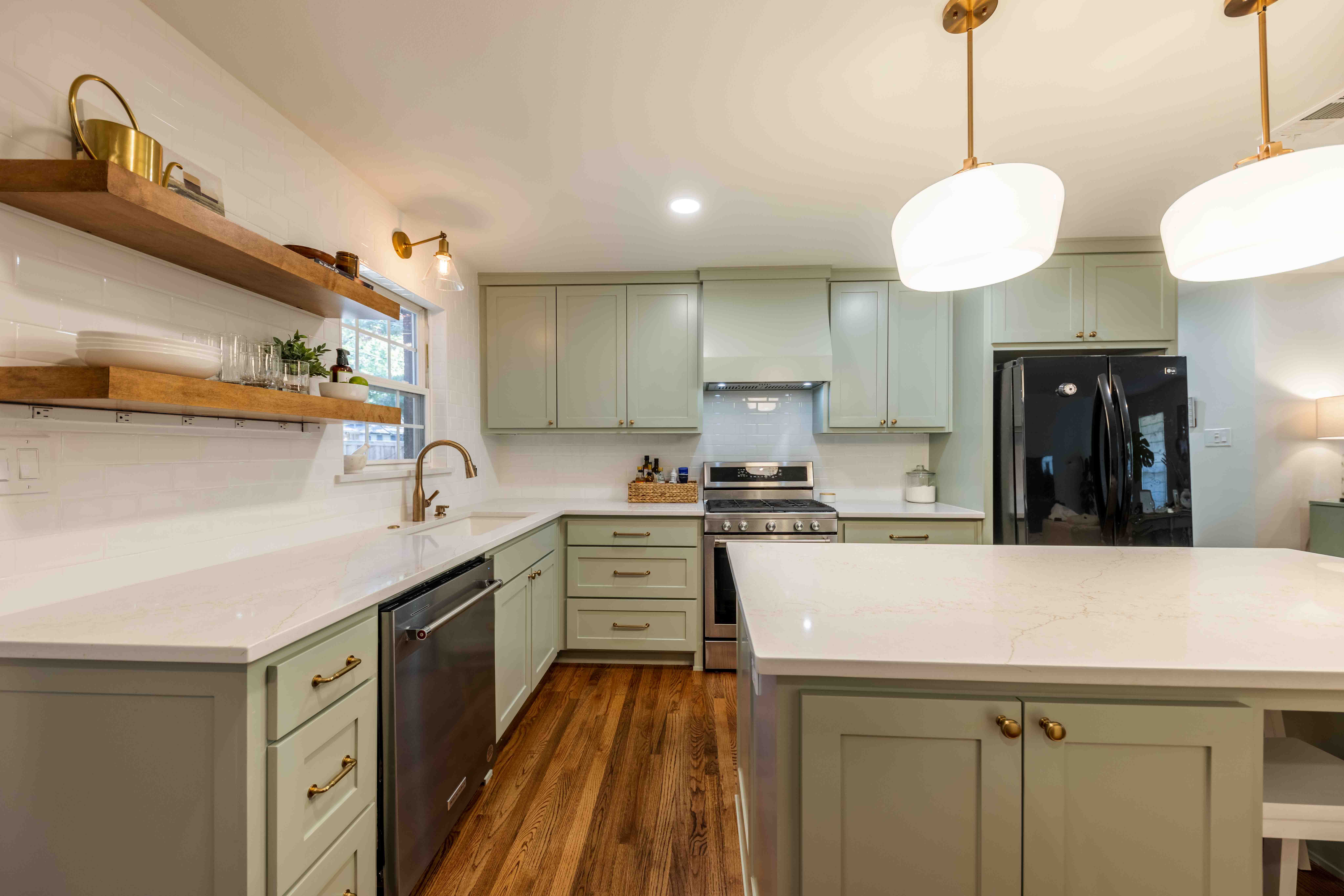 Modern kitchen with light green cabinets, white countertops, wooden floor, and hanging pendant lights.