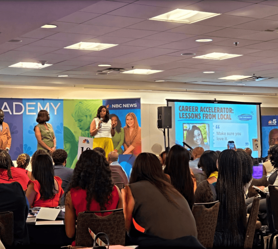 A woman speaks on stage in front of a large audience at a career event, with a screen displaying lessons from local experts.