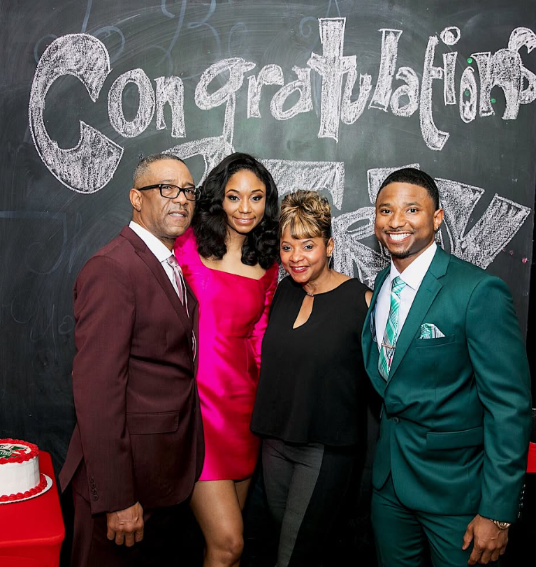 Four people standing in front of a chalkboard with 'Congratulations' written on it, smiling, dressed in formal attire.