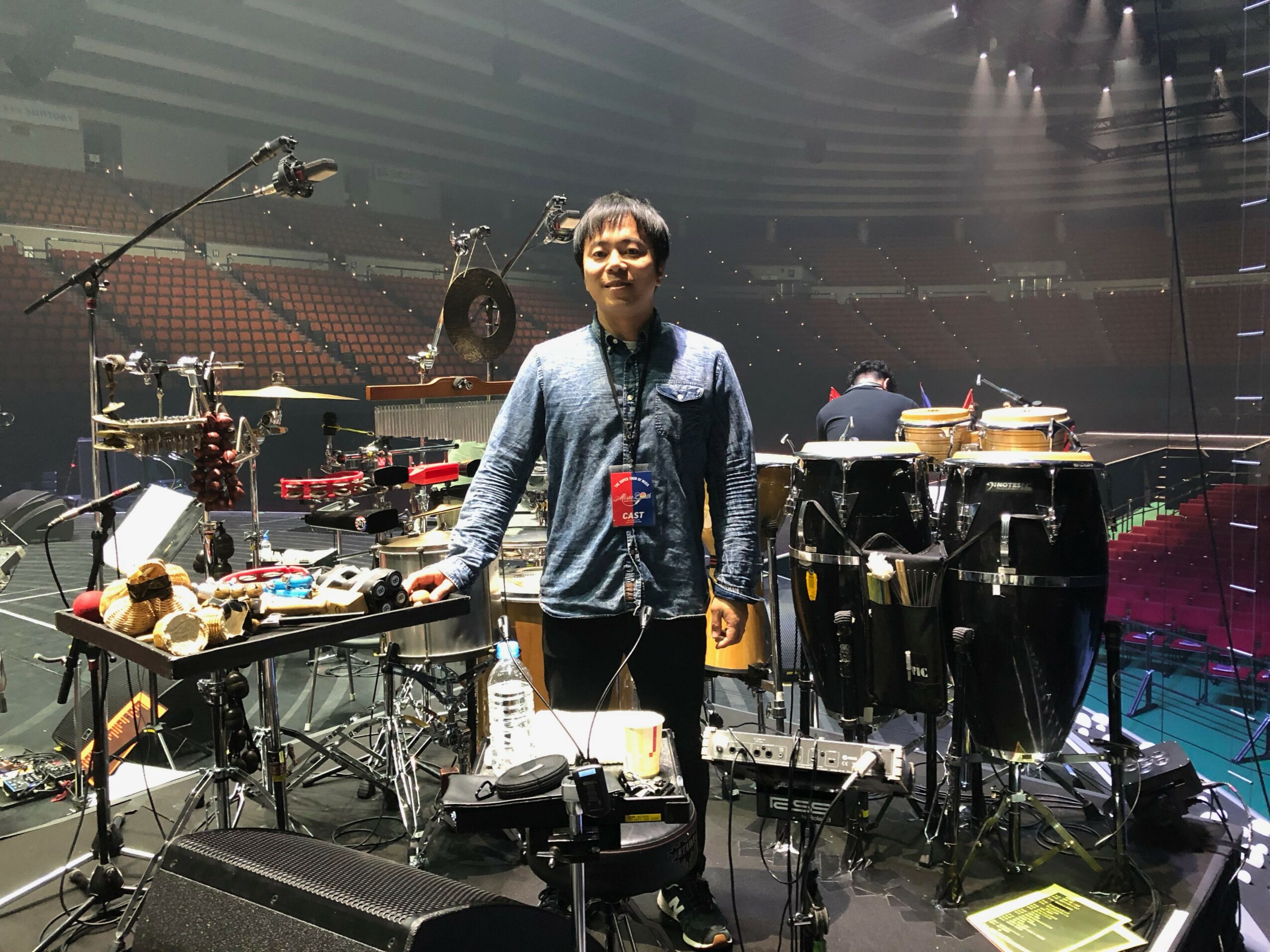 Person standing on stage with musical instruments and equipment, empty auditorium in background.